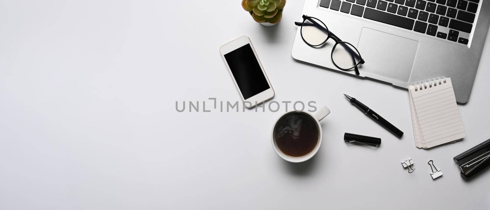 Top view computer laptop, smart phone, coffee cup and notebook on white table.