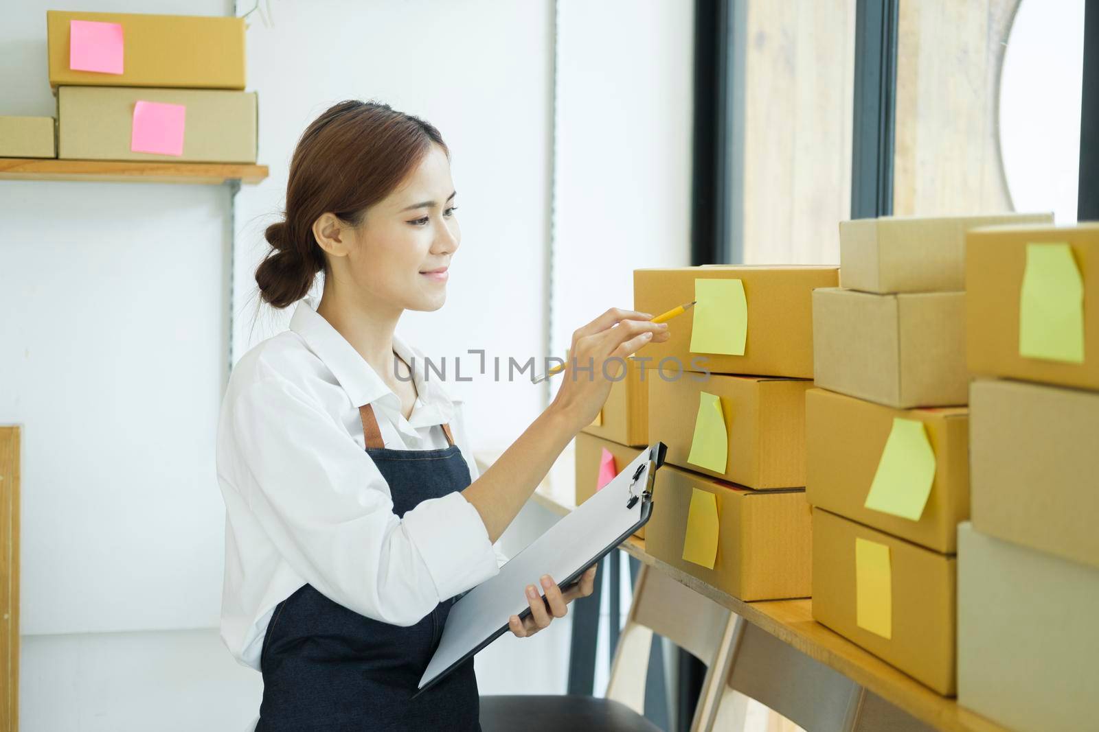 Asian female small online business owner packing boxes on table and checking retail order preparing for shipment. Online business, e-commerce concept.