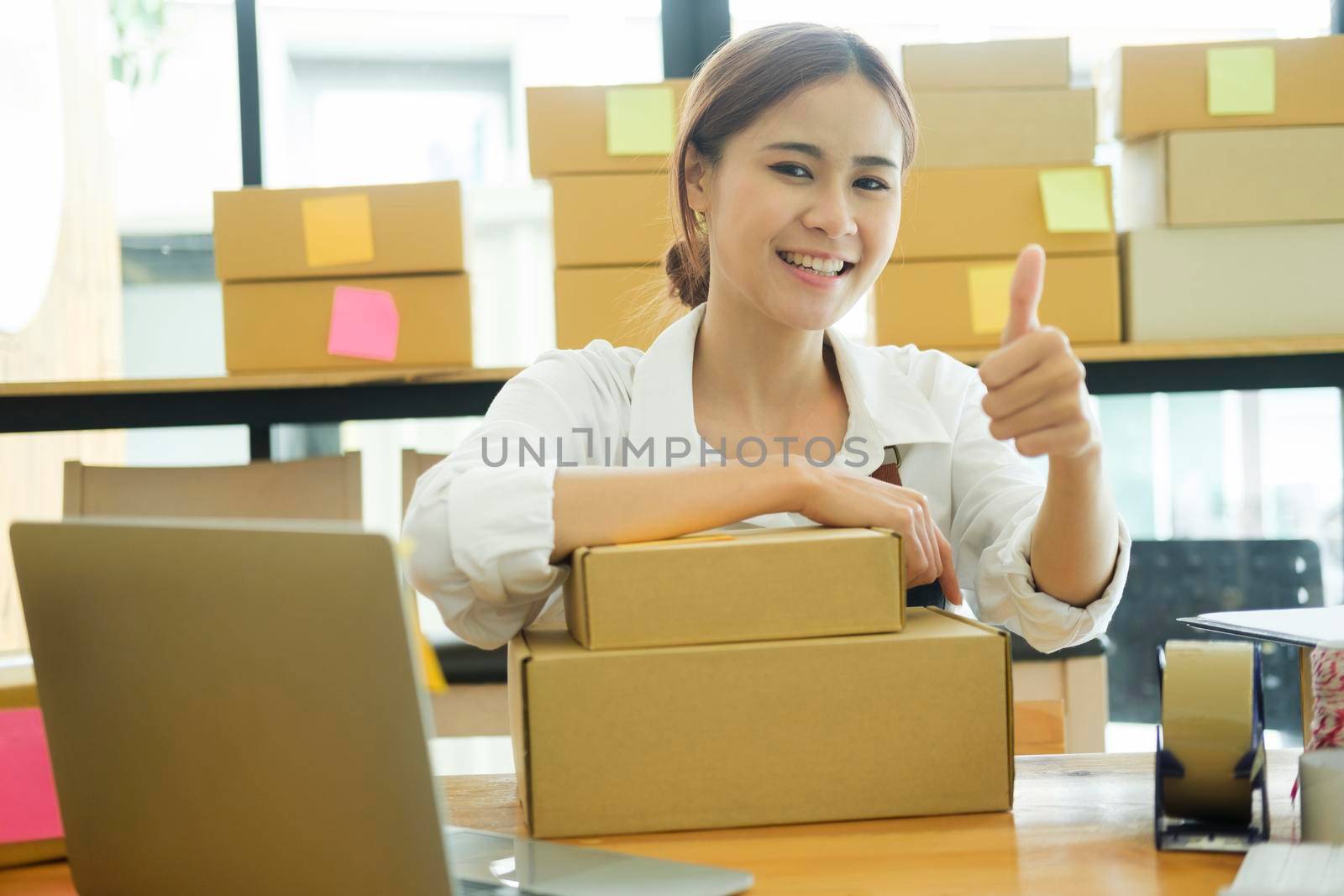 Asian female online business owner happy selling products online and giving thumb up gesture. Woman showing doing good work at her online business and showing thumb up. Online business concept.
