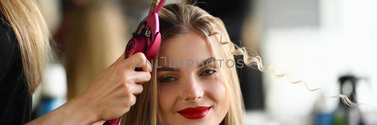 Master woman hairdresser curls hair of girl in beauty salon by kuprevich