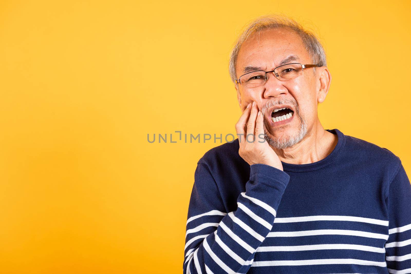 Dental pain. Asian unhappy elder man problems with gum pain studio shot isolated on yellow background, Portrait senior old man sad hand touching cheek suffering from toothache, dental healthcare