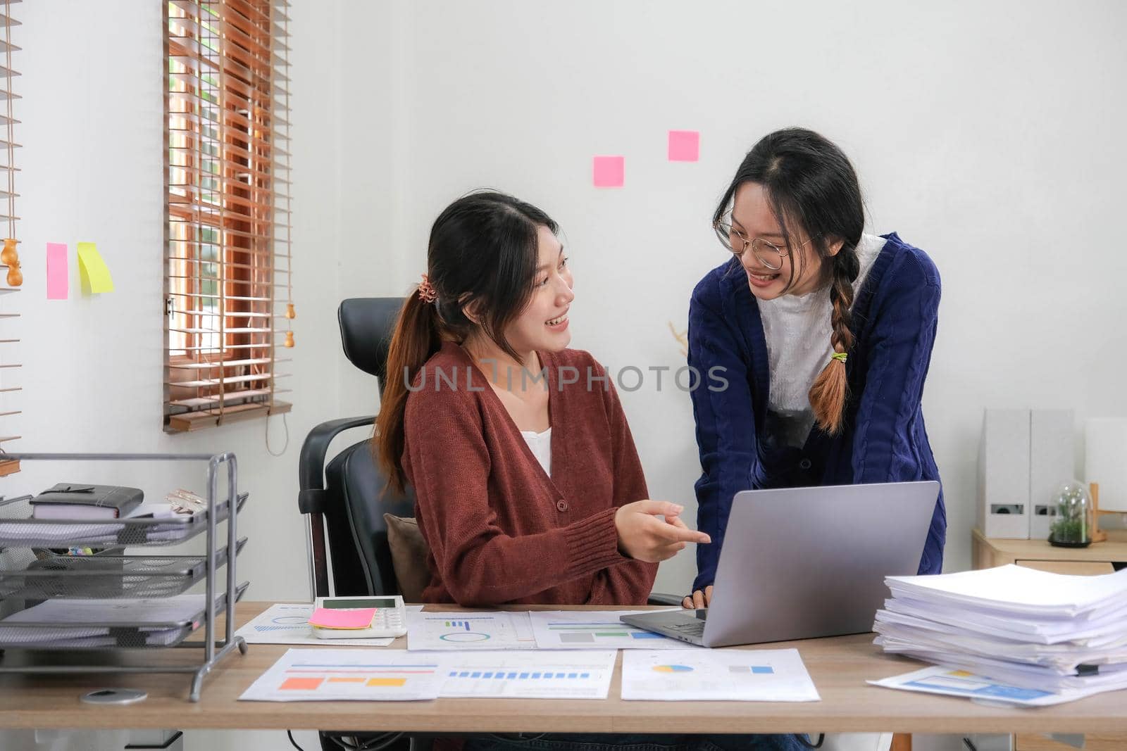 Two young Asian woman discuss investment project working and planning strategy. Business people talking together with laptop computer at home. by wichayada