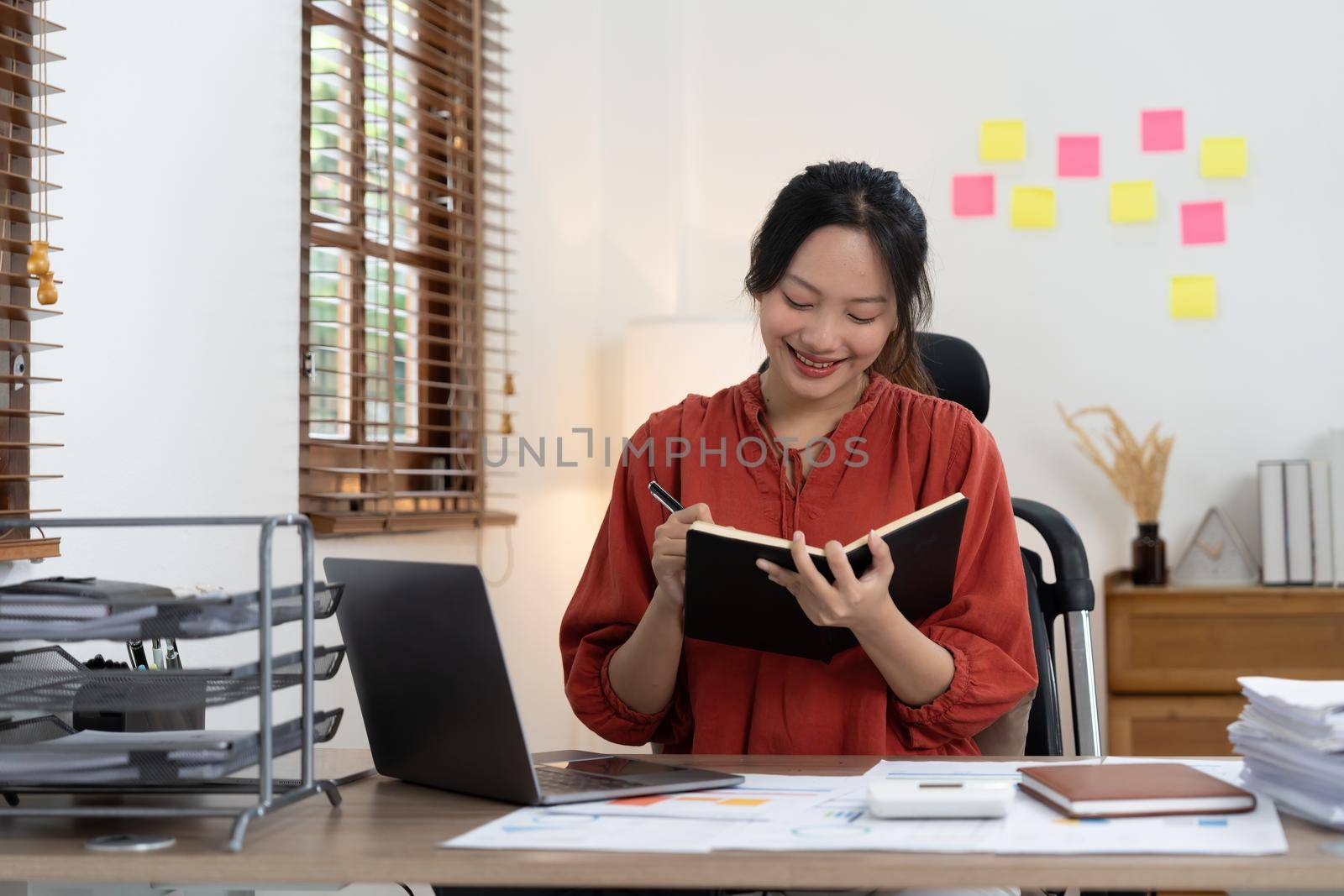 businesswoman or accountant taking note and working on calculator and laptop computer to calculate business data during make note at notepad, accountancy document at office.