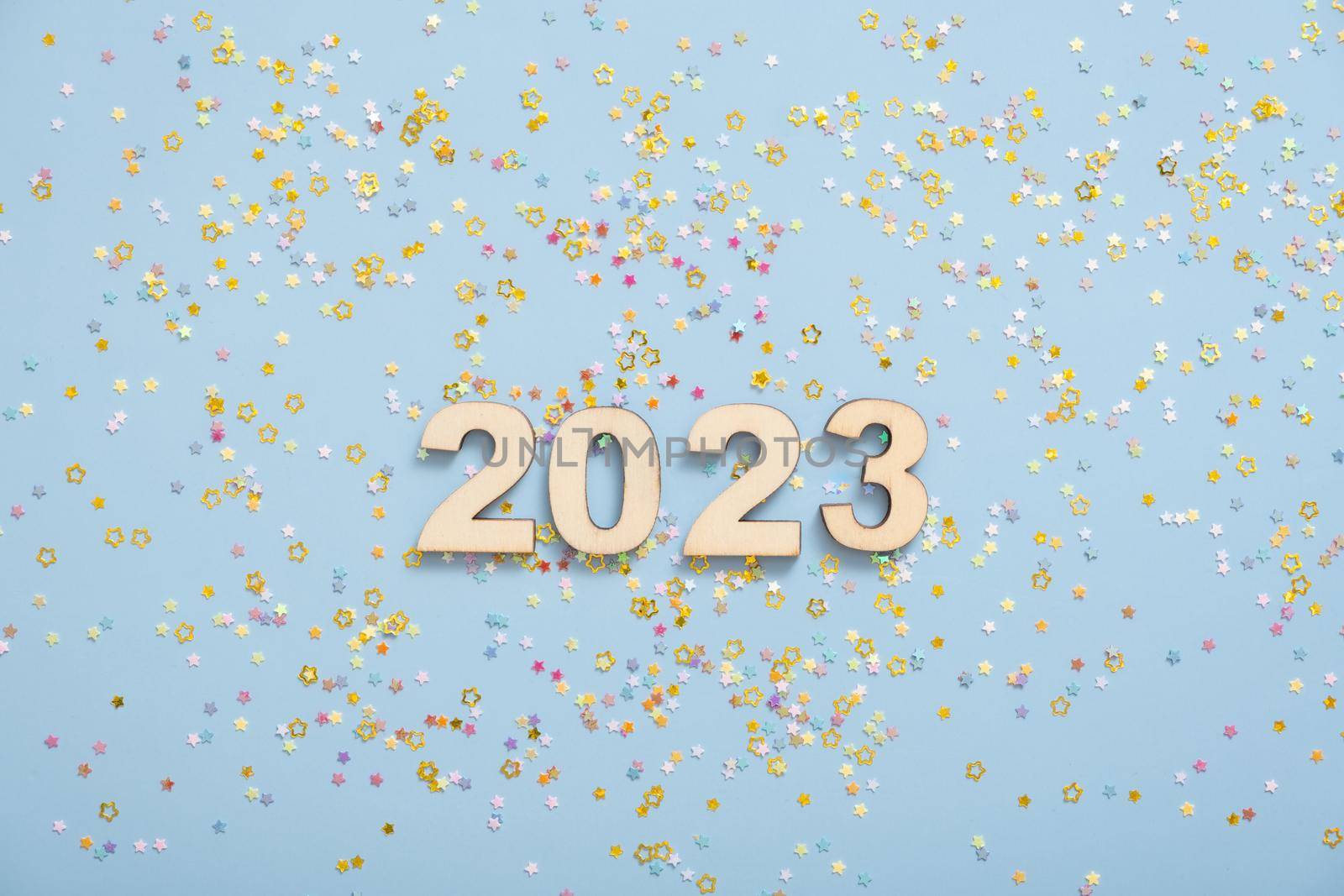 Wooden numbers 2023 on a pastel blue background with stars. Festive New Year background.