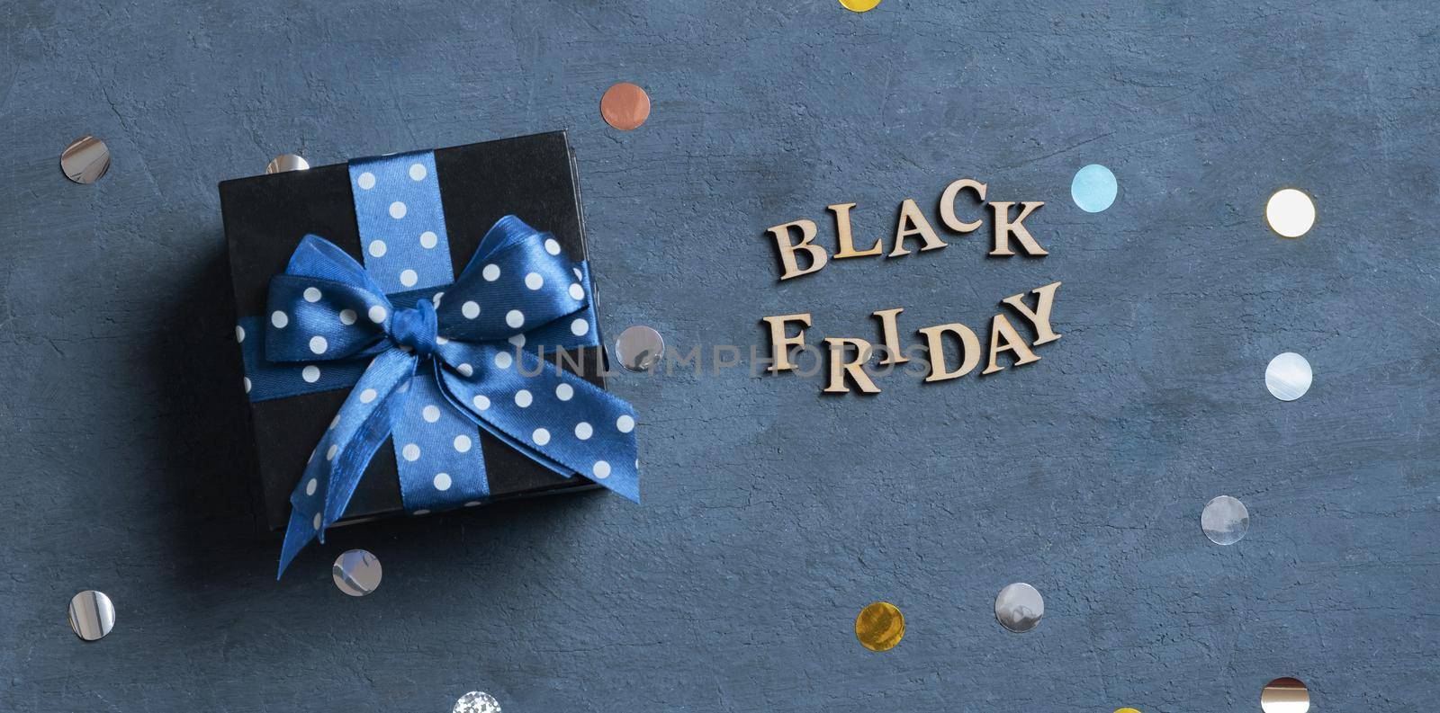 Black Friday text with black gift box flat lay on dark cement background. Top view.