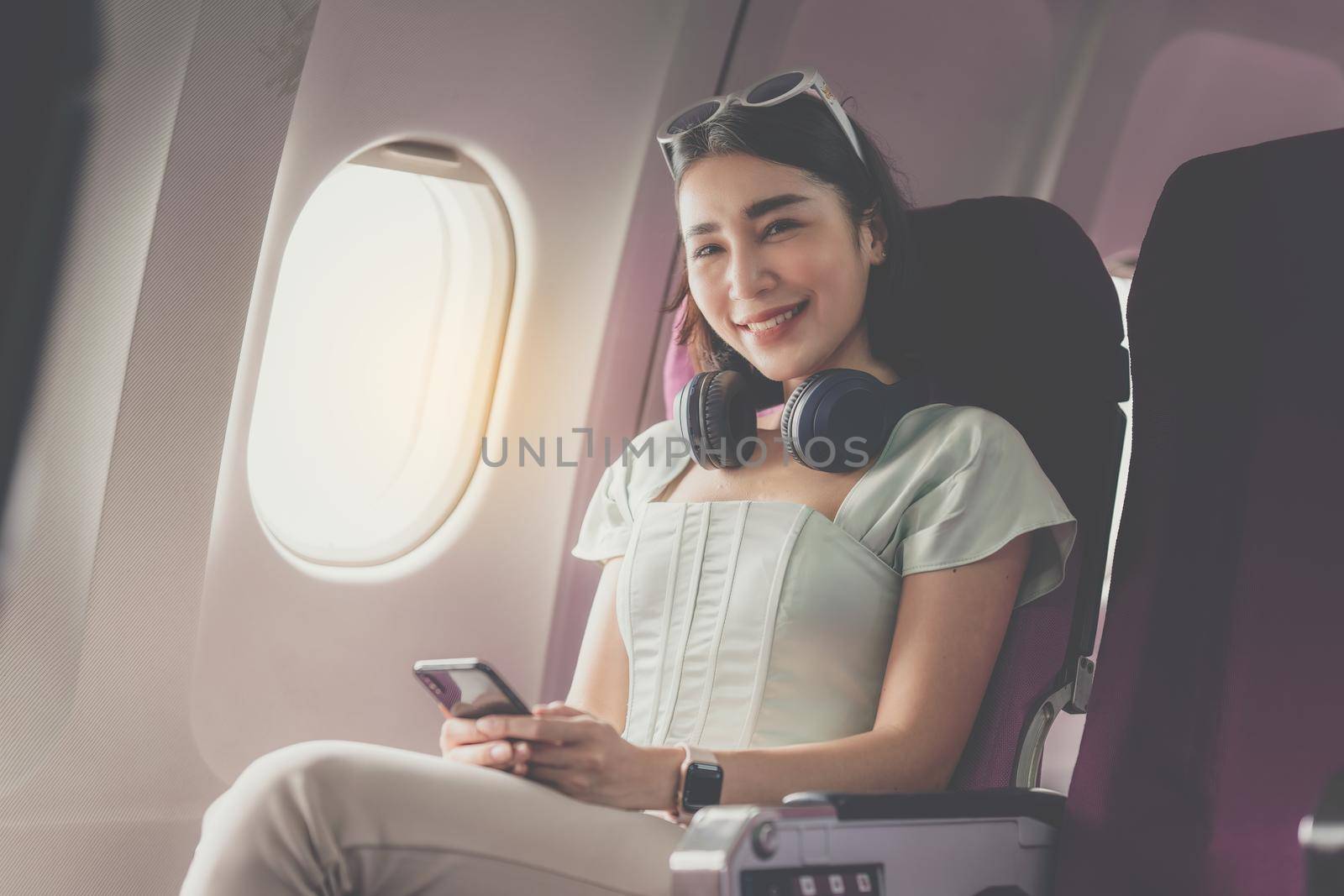 Joyful asian woman sits in the airplane and using mobile phone while go to travel by itchaznong