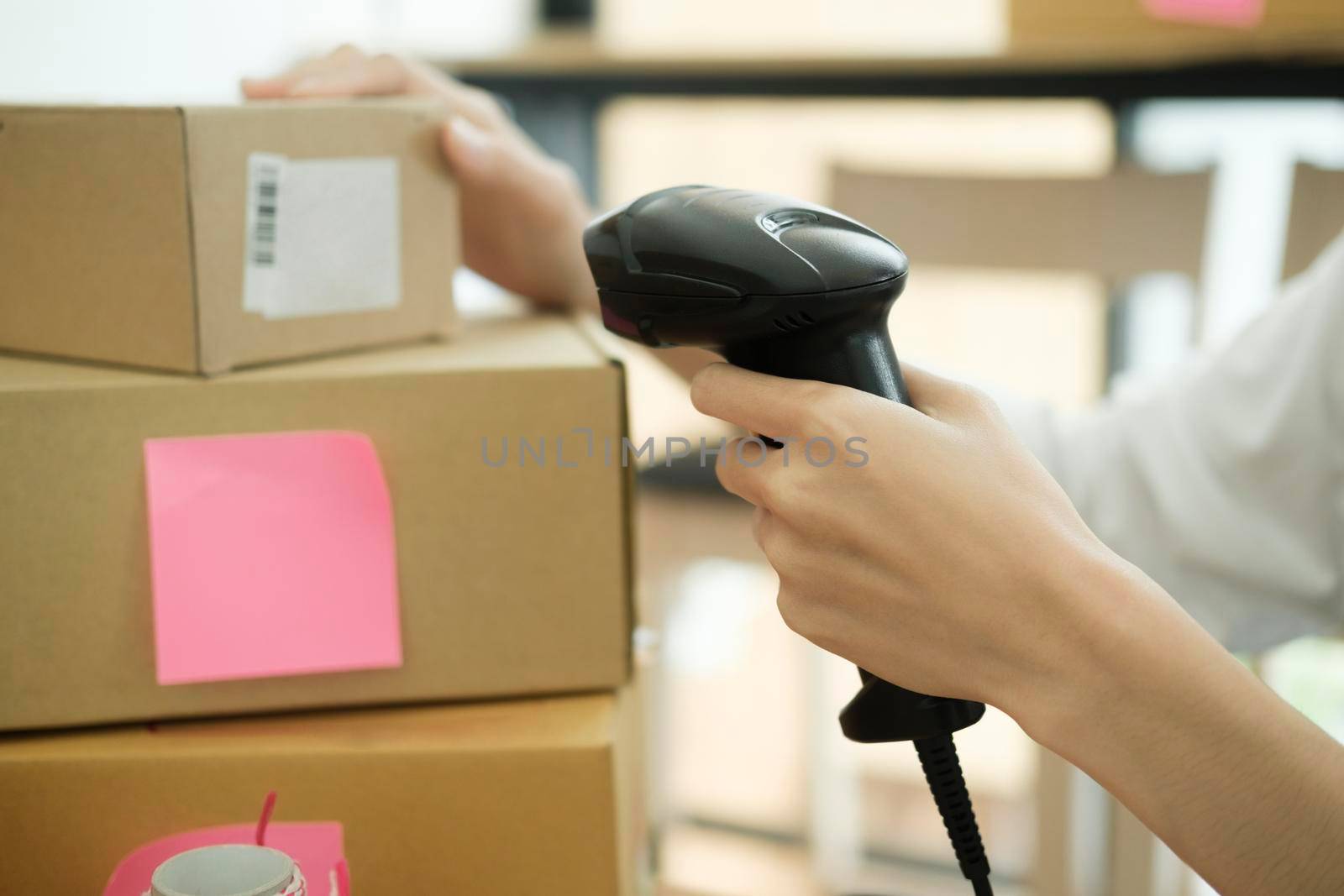 Female small online business owner holding scanner scanning parcel barcode tag before shipment at workplace. Woman selling products online, scanning parcel barcode. Online business concept.