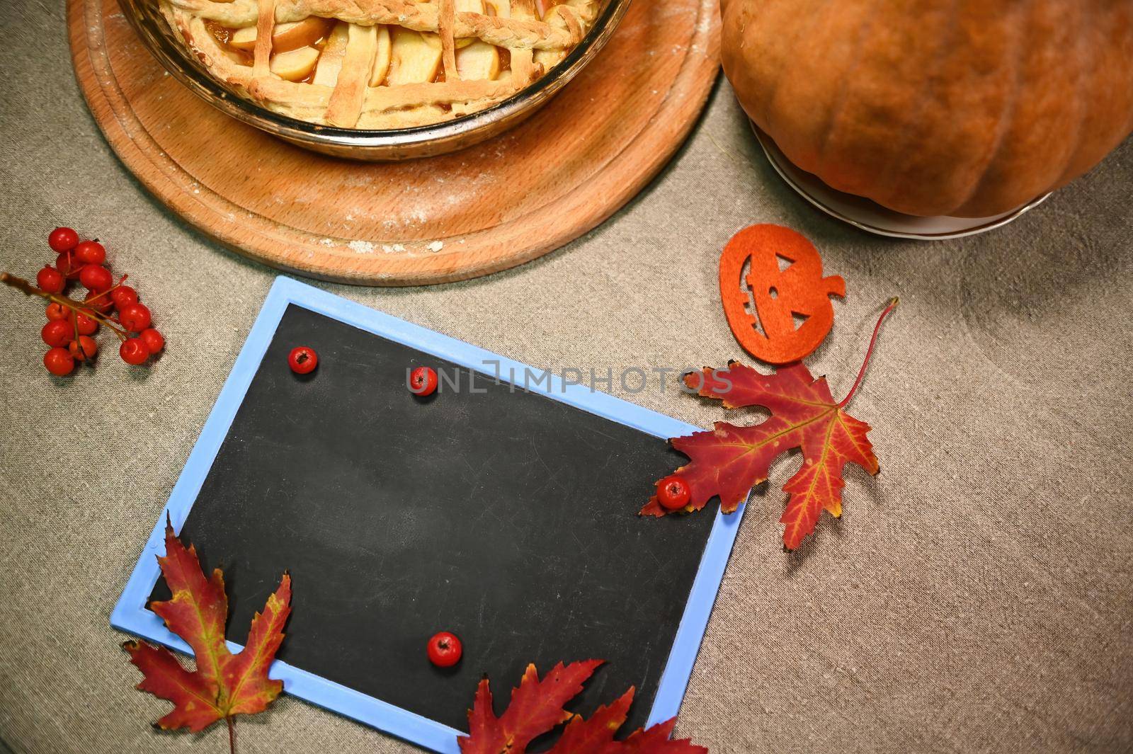 Top view. A chalkboard with copy space for promotional text, autumn maple leaves and Thanksgiving pumpkin pie on tabl by artgf