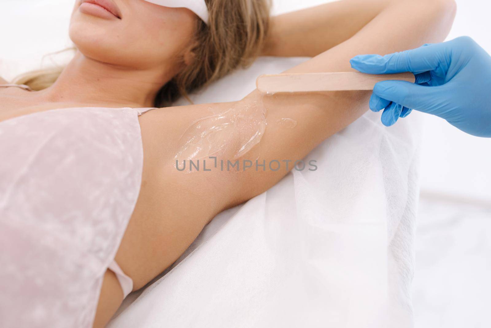 Woman beautician in blue glowes applies contact gel on the armpit of a woman for laser hair removal in cosmetology studio. Close up by Gritsiv