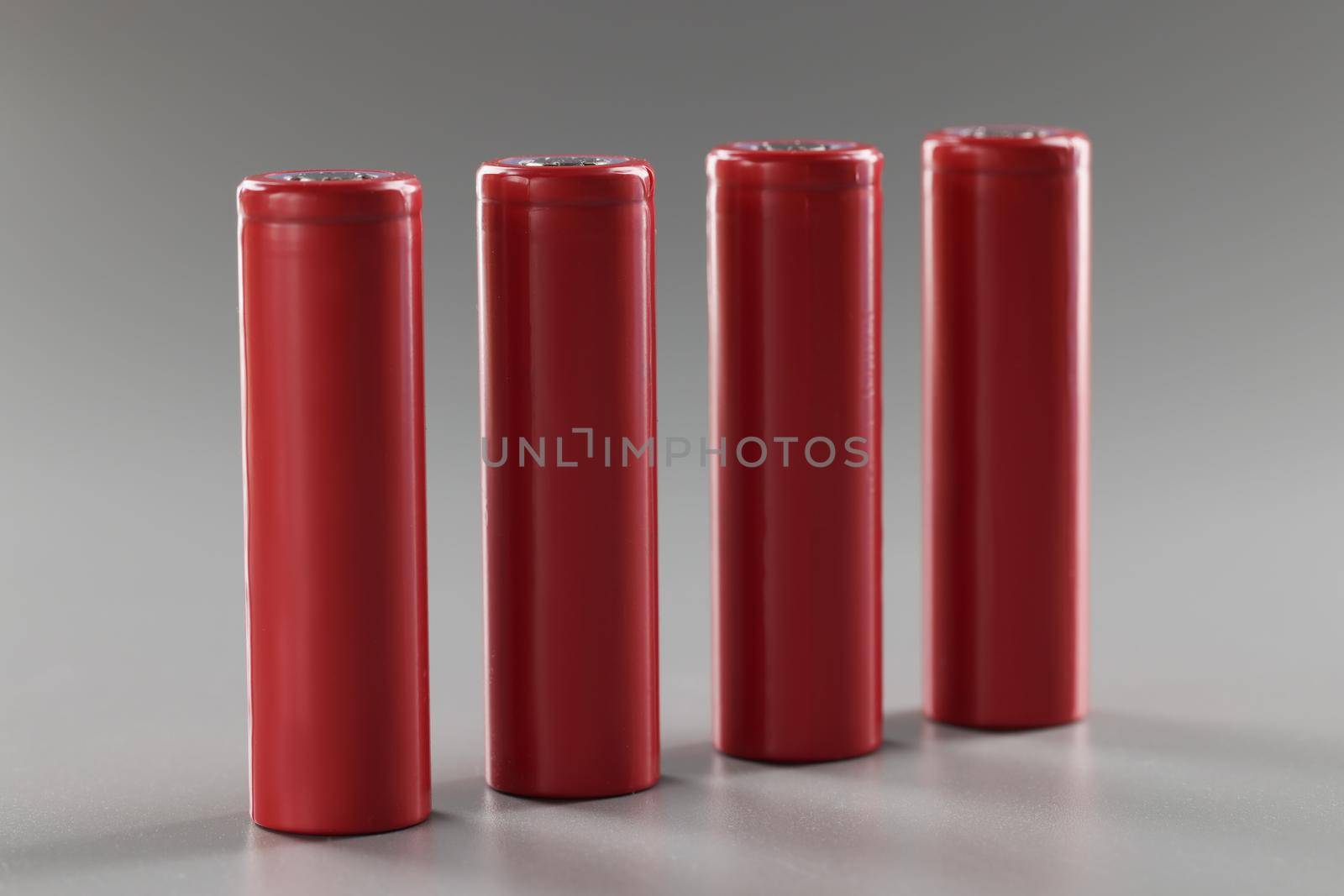 Red batteries stand in a row on a gray background, close-up. Rechargeable alkaline battery. Disposal lithium material