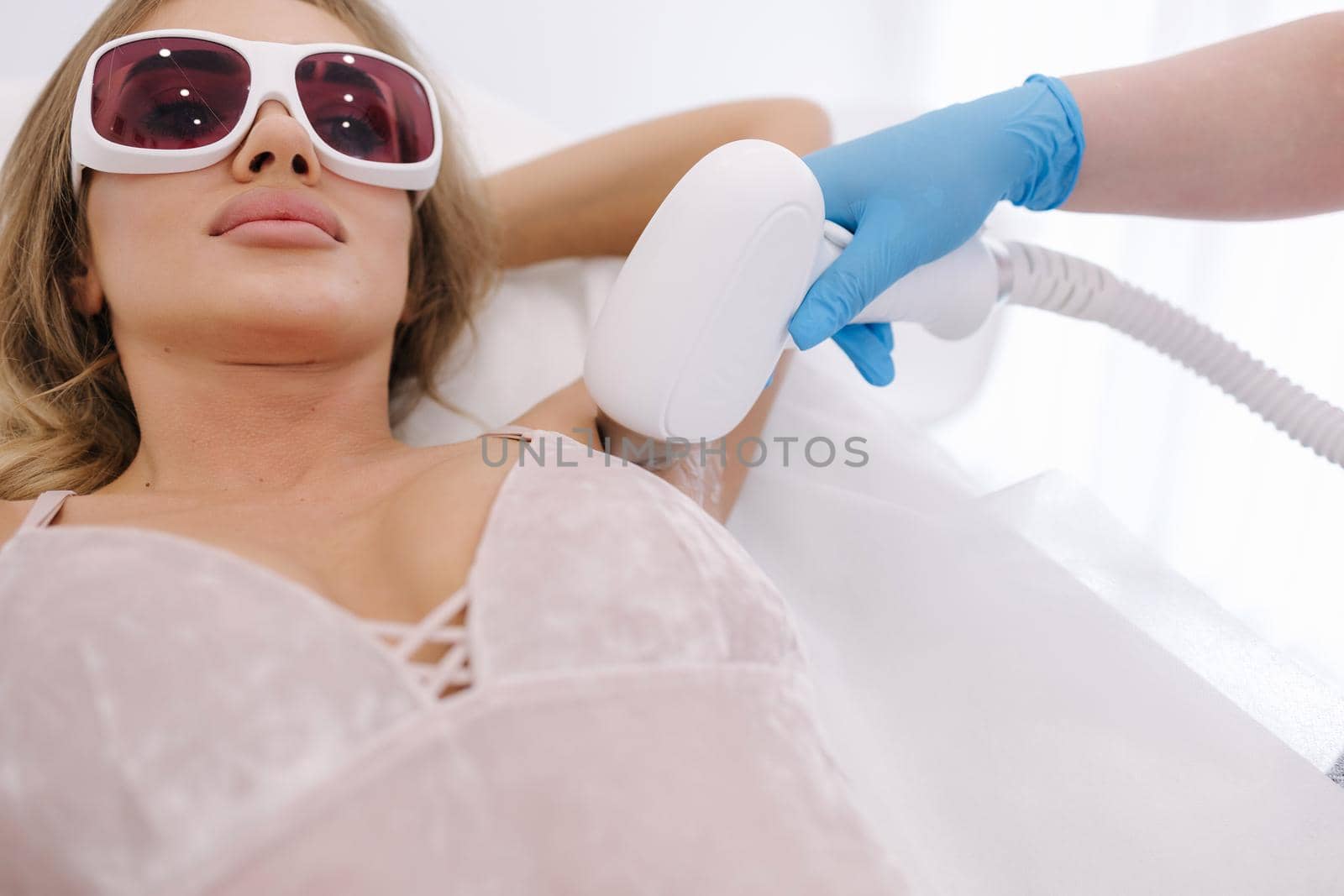 Beautician doing epilation on female's armpit in beauty center. Woman receiving laser light hair removal treatment for hairless smooth skin at cosmetology salon by Gritsiv
