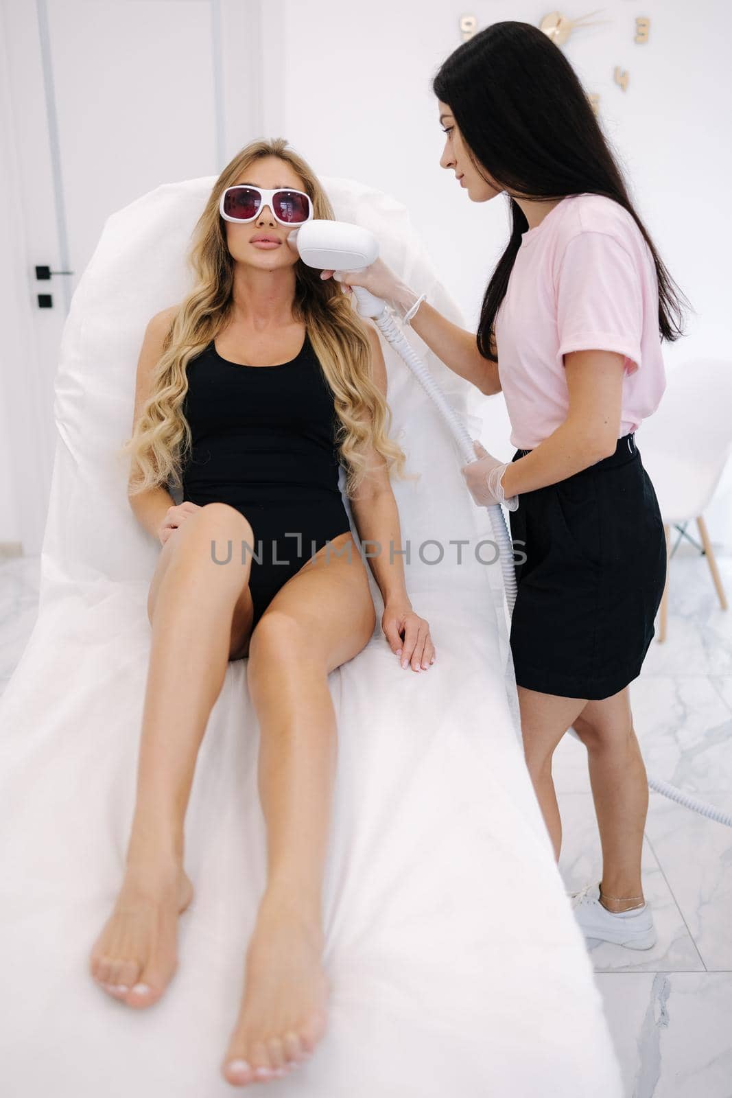 Beautician doing epilation on the face of a beautiful woman in beauty center. Female receiving laser light hair removal treatment for hairless smooth skin at cosmetology salon. Model in protective glasses by Gritsiv