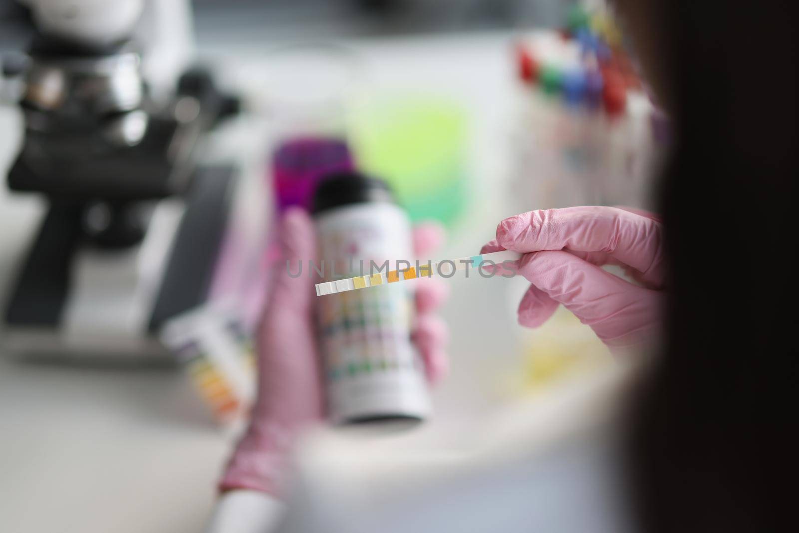 Gloved hands in the laboratory hold a litmus test strip, close-up, blurry. Bio samples for analysis. Ketones urine test