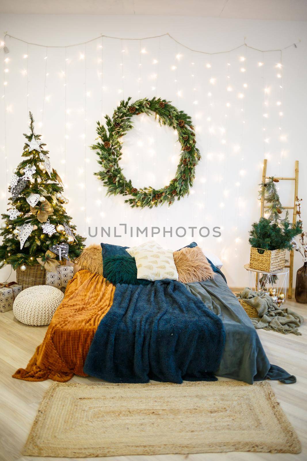 Christmas festive interior in gray and white colors. A round green wreath hangs on the wall. A bed covered with cozy blankets stands in a house decorated with a garland.