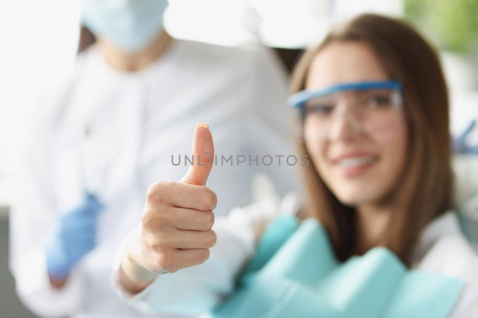 A woman at the dentist shows a thumbs up gesture, blurry, close-up. Professional dental care, satisfied patient
