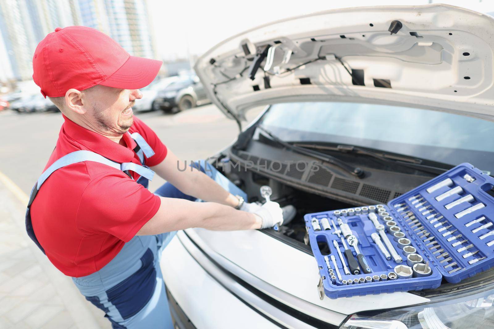 A man in a uniform on the street fixes a breakdown in a car, close-up. Car repair tools, call from repairman