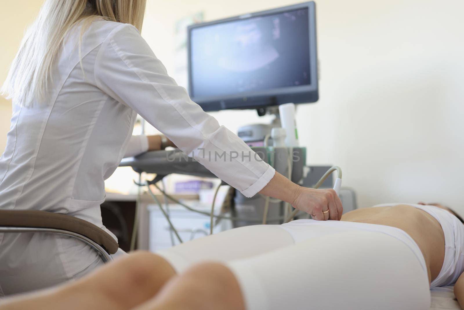 Woman doctor makes an ultrasound of the abdomen of a woman, rear view. Clinical consultation and diagnosis of diseases