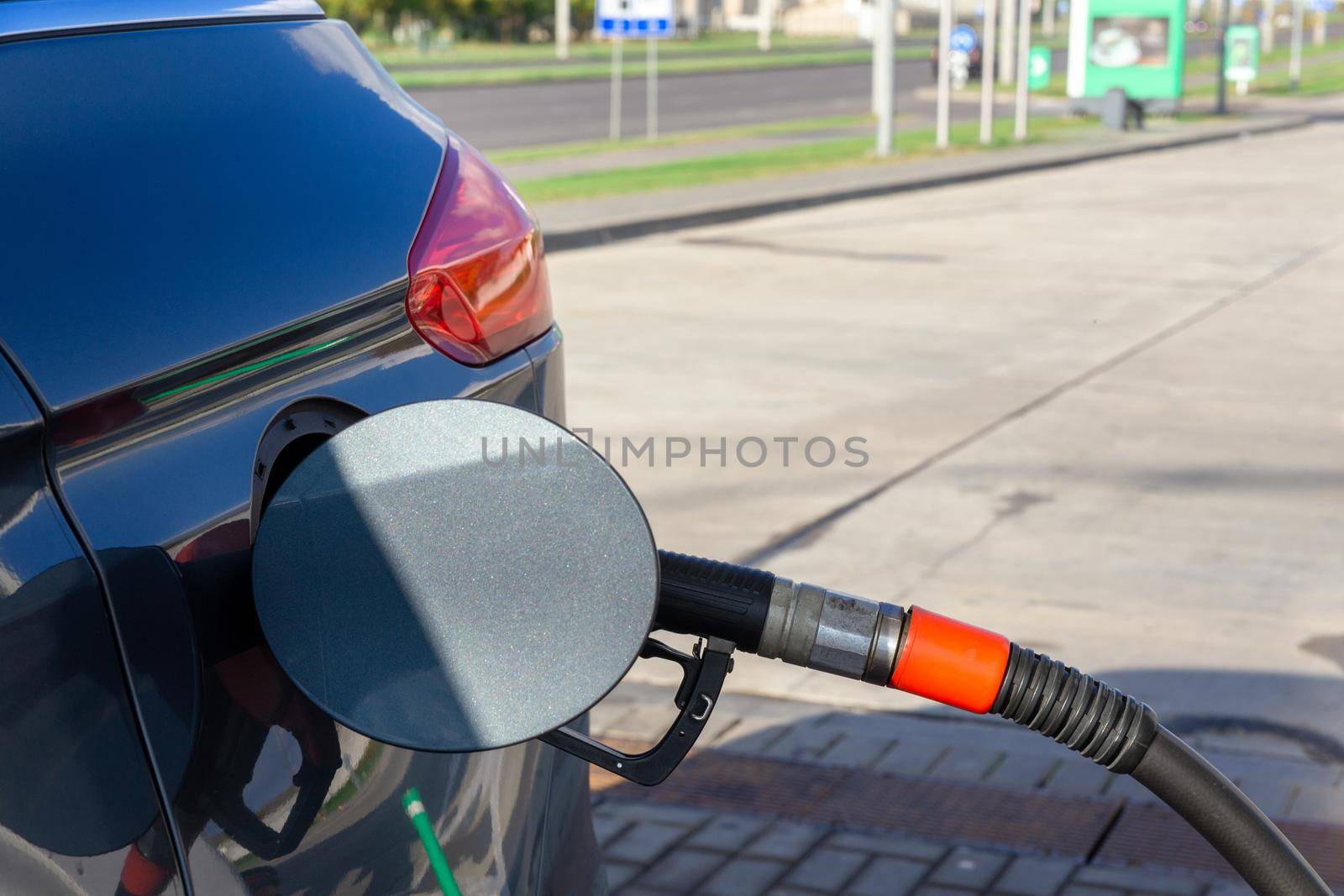 Fuel nozzle to refill fuel in car at gas station. Red fuel dispenser on gray car in petro station.