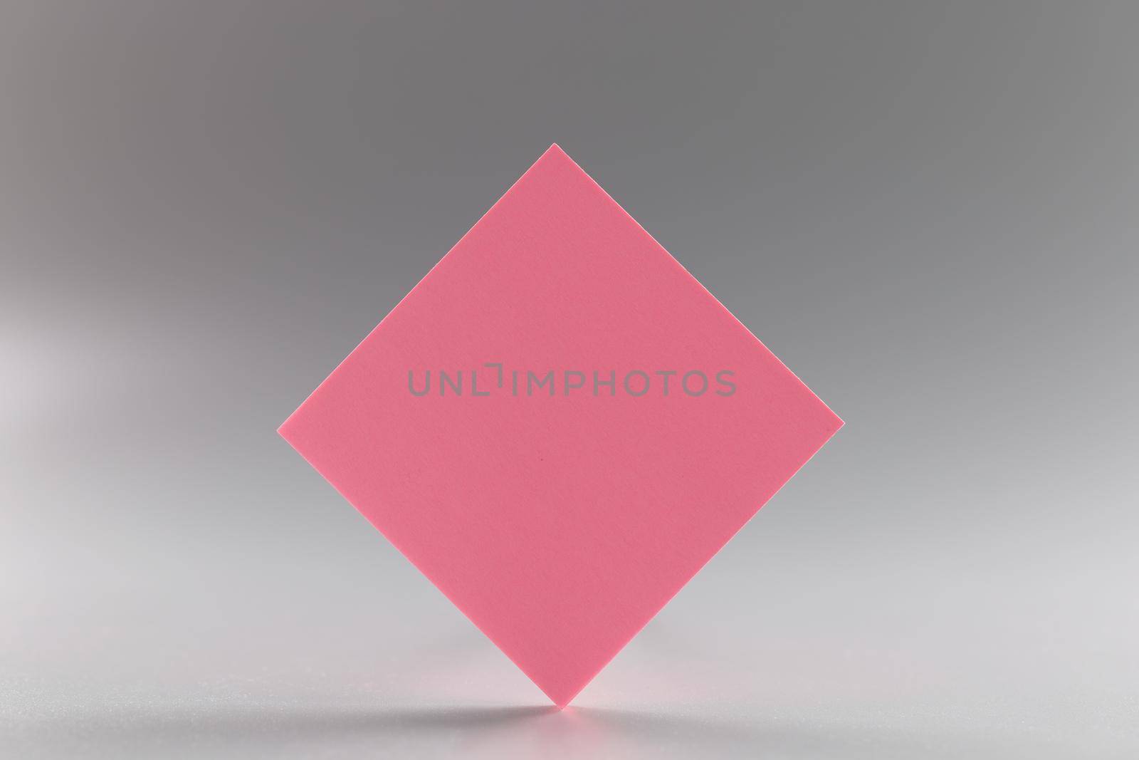 Pink blank paper rhombus on a gray background, close-up. beautiful design element, sheet sticker, branding