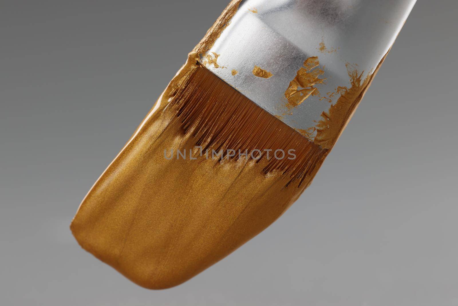 Brush with gold paint on a gray background, close-up. Shiny golden texture of paint on the bristles of a painting brush