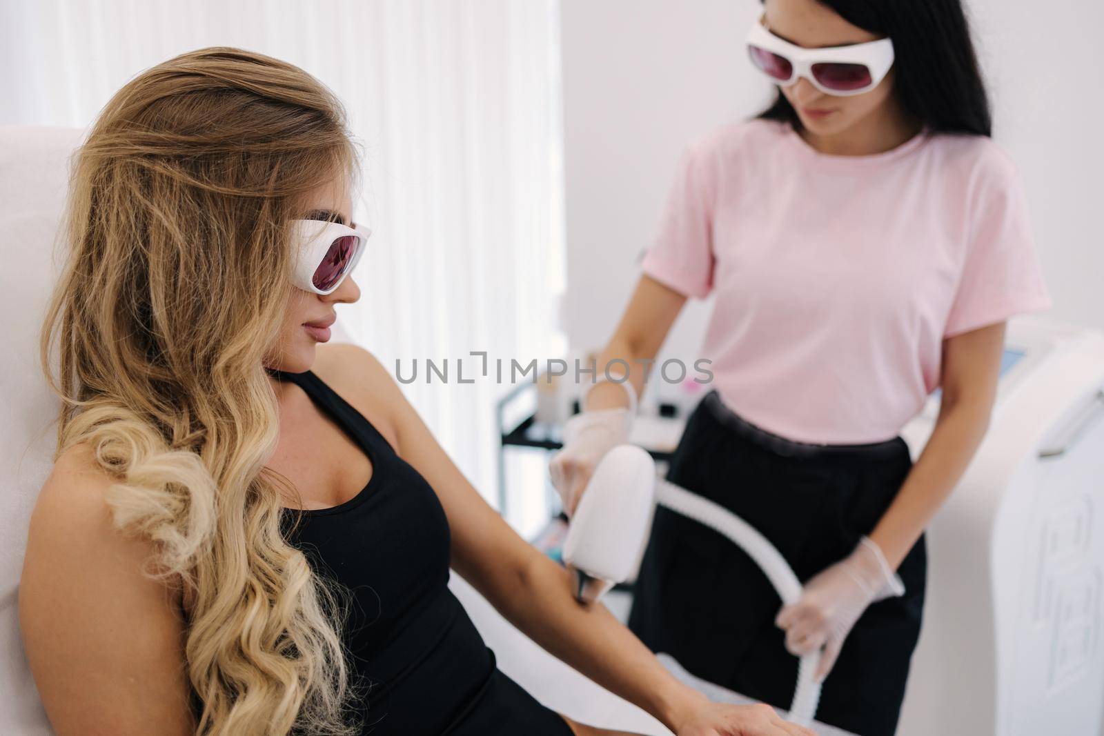 Cosmetology. Beautiful woman receiving laser hair removal procedure at beauty salon. Beautician doing beauty treatment for female arm at spa salon. Protective glasses by Gritsiv