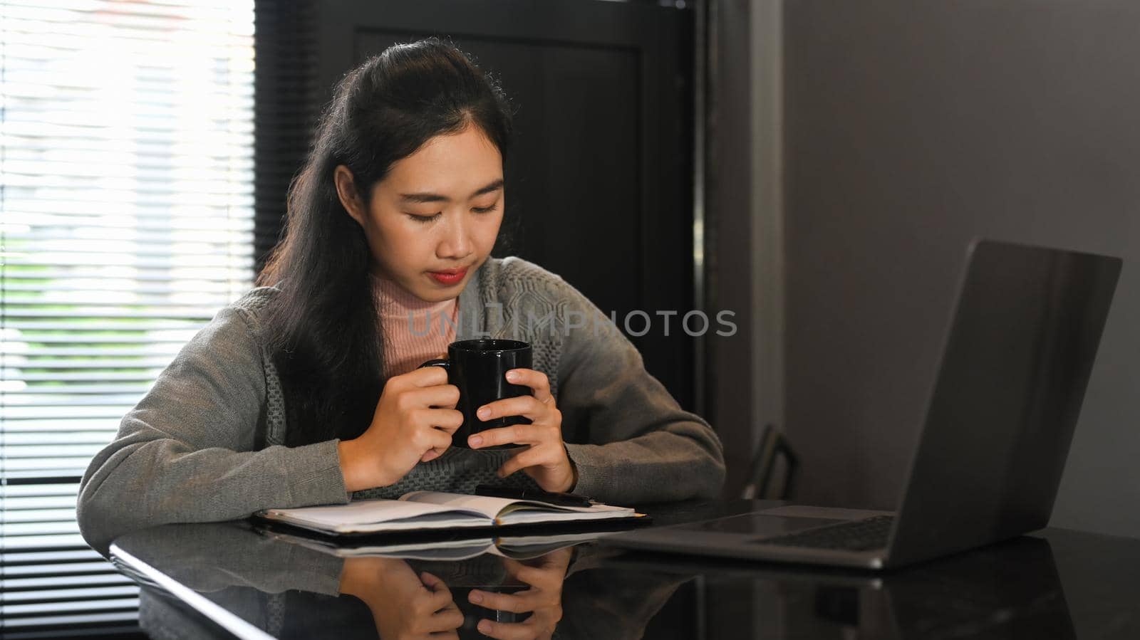 Young woman holding cup of hot coffee using laptop computer at comfortable home.