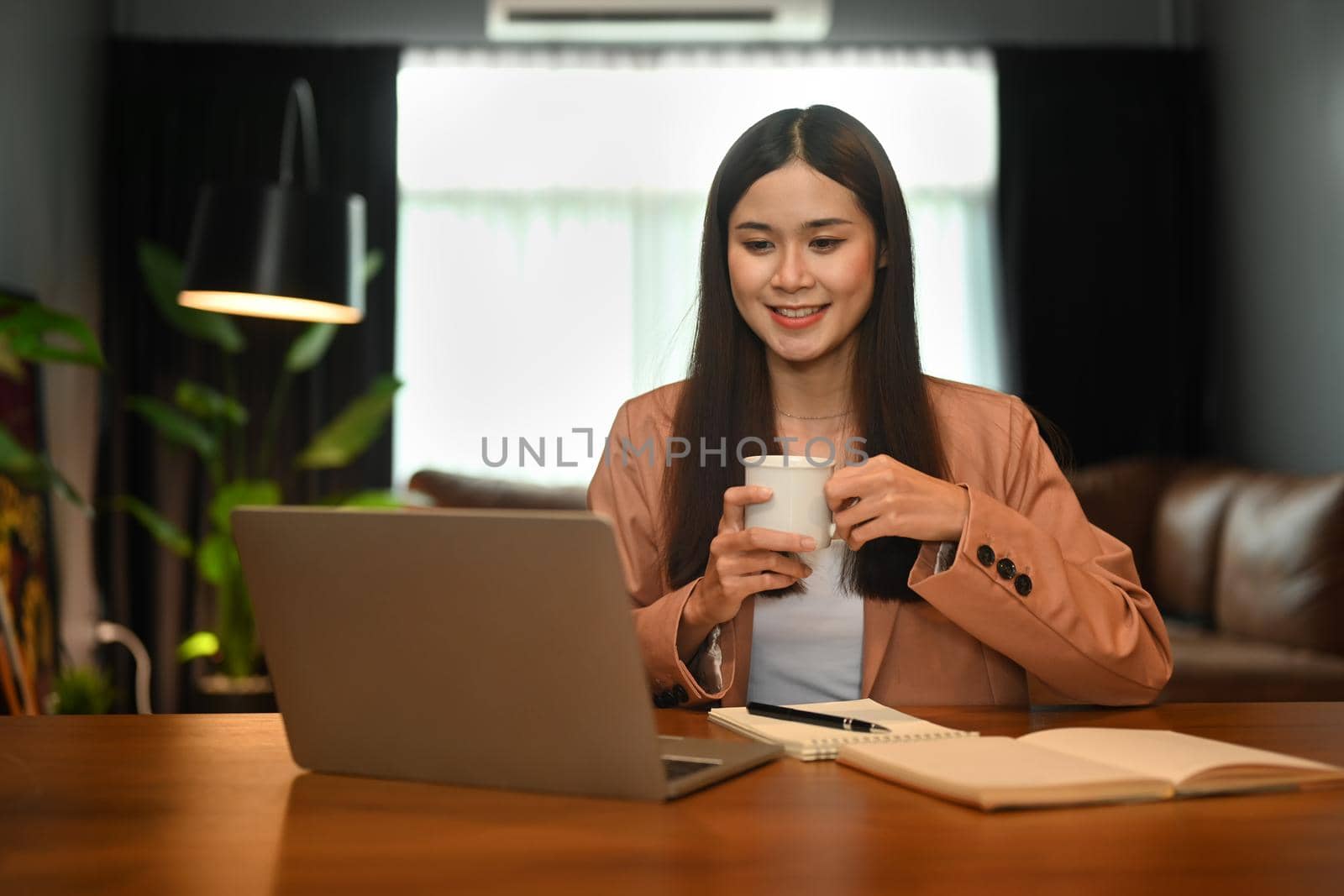 Charming asian businesswoman drinking coffee and reading email on her laptop computer.