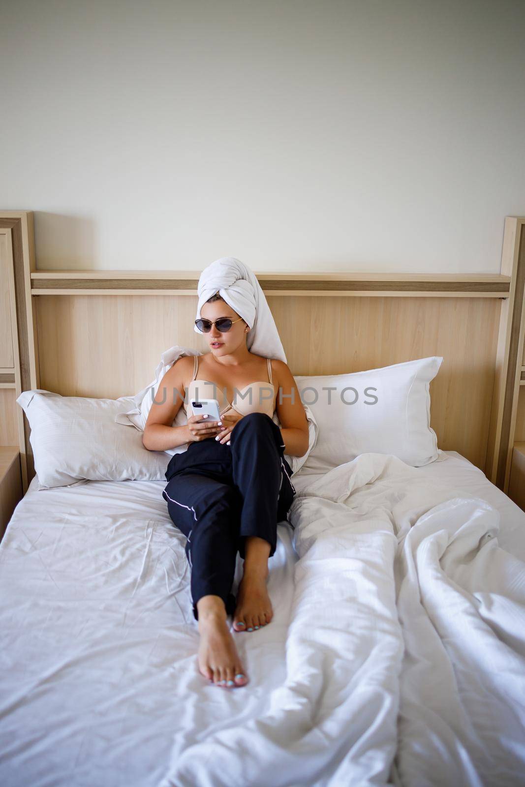 A beautiful young woman is lying in a large snow-white bed with a towel on her head.