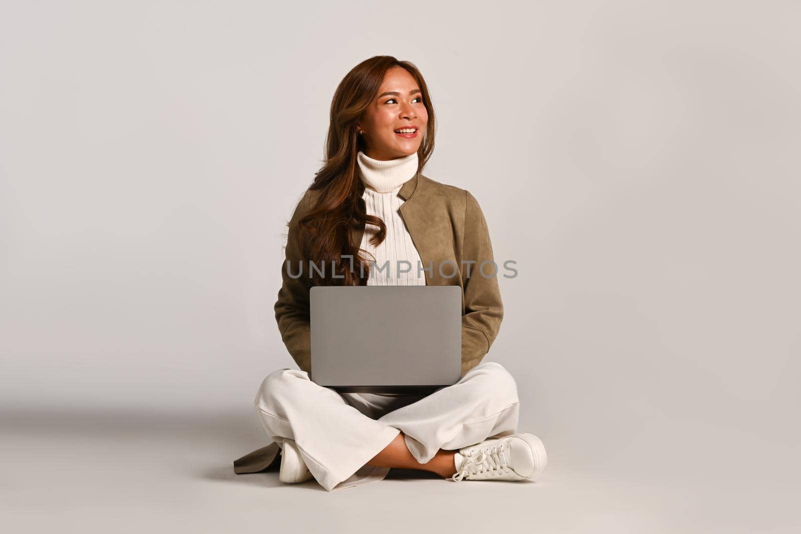 Beautiful woman in trendy clothes sitting with laptop over white studio. People and technology concept.