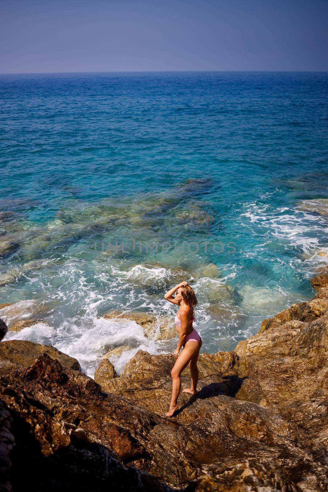 Young beautiful woman in a swimsuit stands on a rocky beach of the Mediterranean Sea. The concept of sea recreation. Selective focus by Dmitrytph