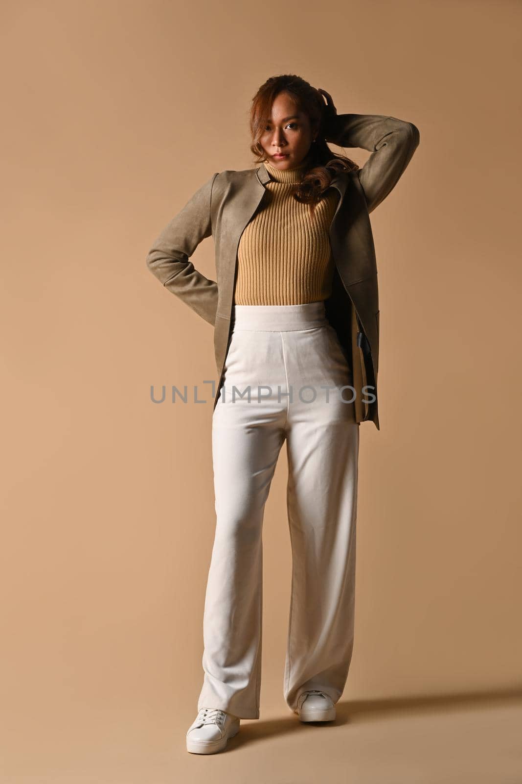 Full length portrait of stylish young woman in trendy clothes standing over beige background. Fashion, beauty concept.