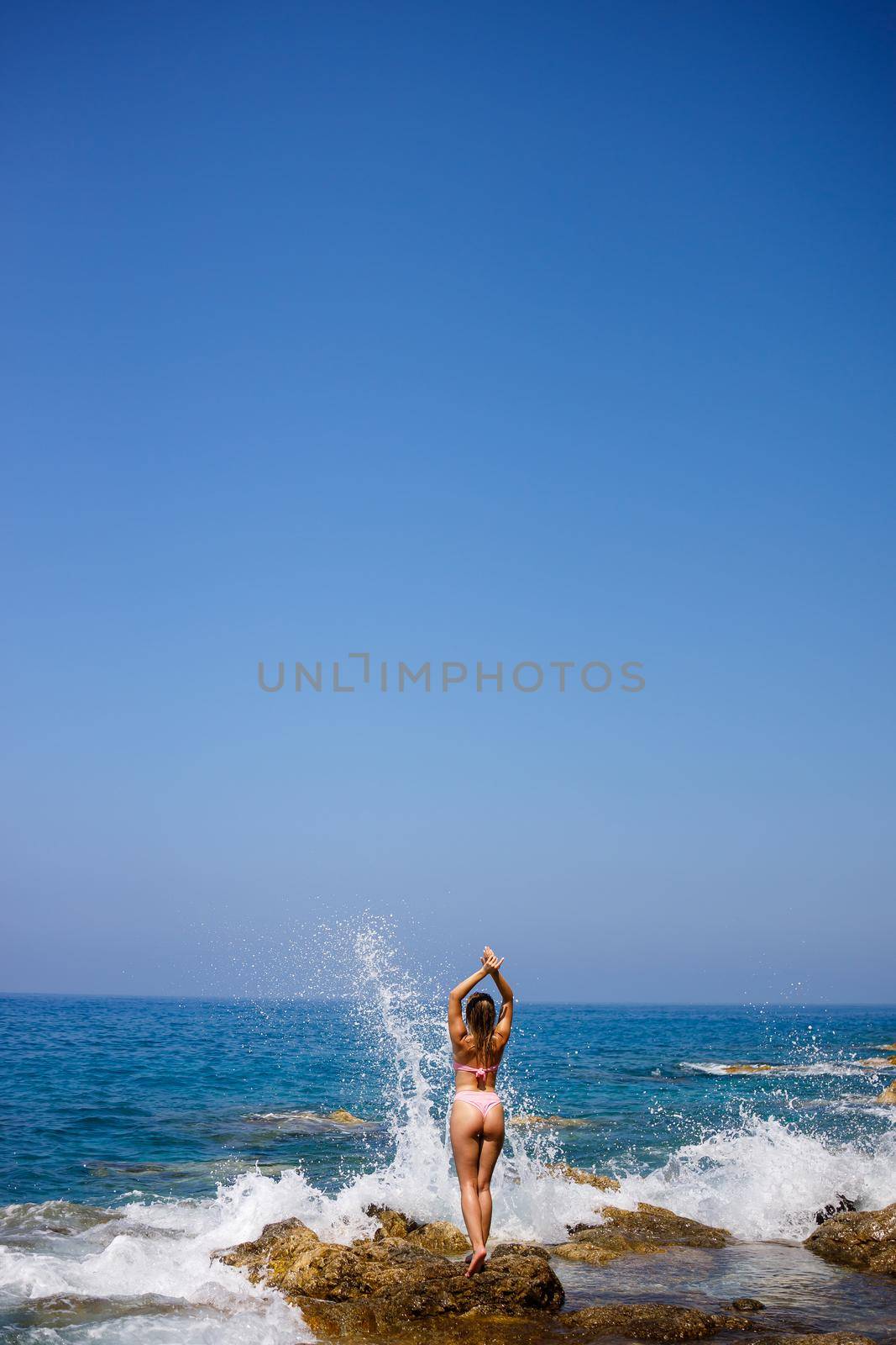 Beautiful young woman in a swimsuit on a rocky beach on a sunny day against the backdrop of waves. Vacation in the summer season. Selective focus