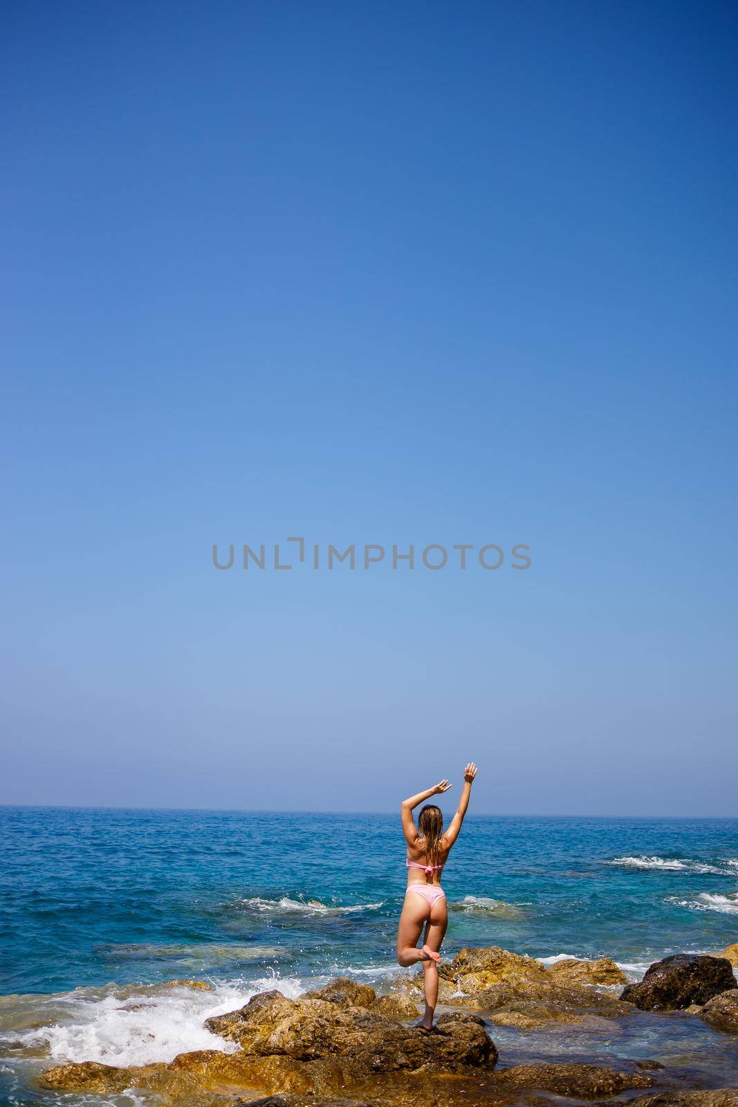 Beautiful young woman in a swimsuit on a rocky beach on a sunny day against the backdrop of waves. Vacation in the summer season. Selective focus