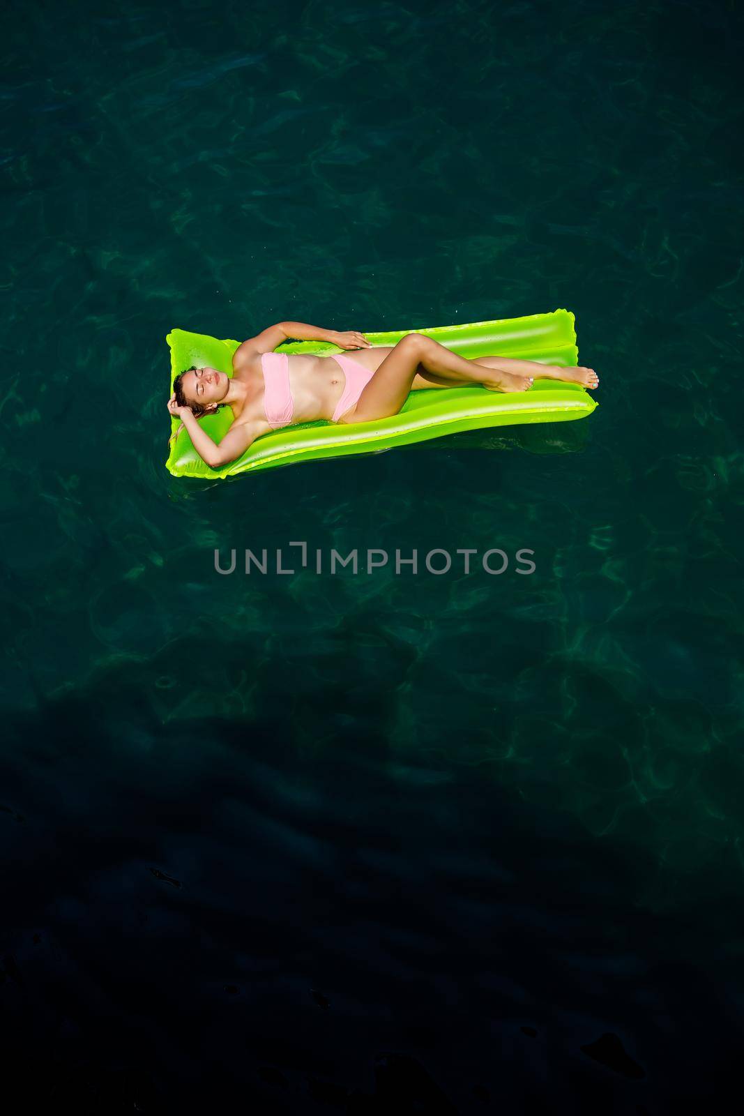 A young woman in a swimsuit swims on an inflatable bright mattress in the sea. Summer vacation concept.