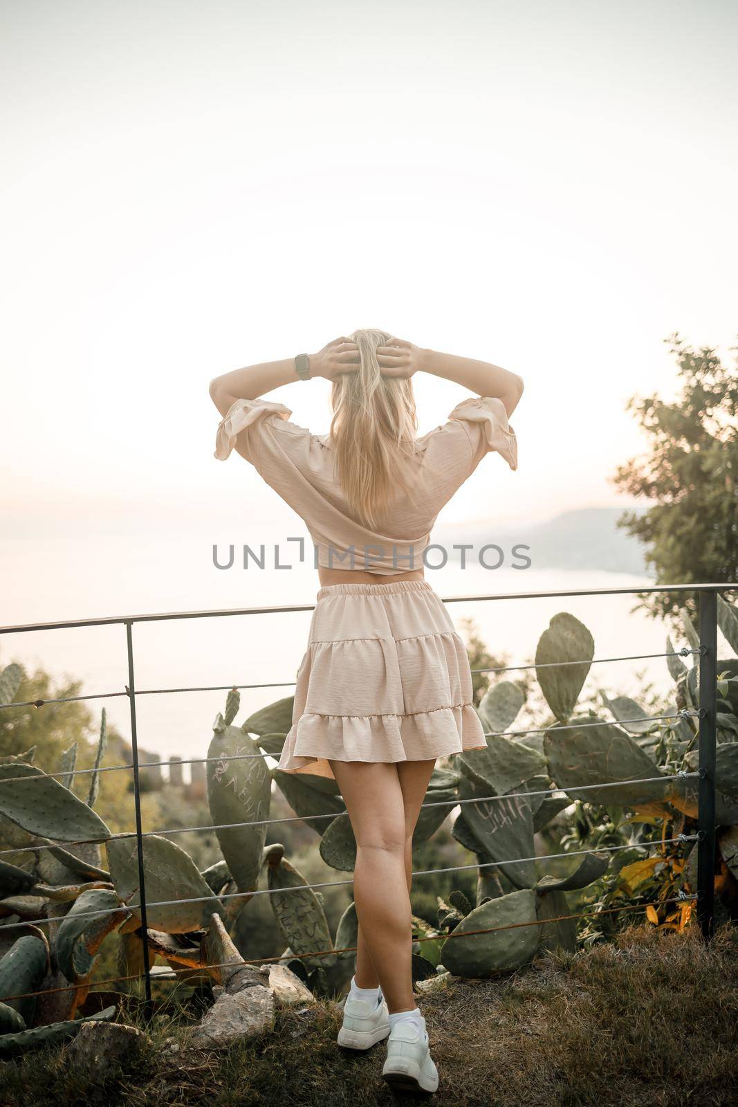 A young beautiful woman in summer clothes stands against the backdrop of a sea view. Incredibly beautiful view of the sunset by the sea by Dmitrytph