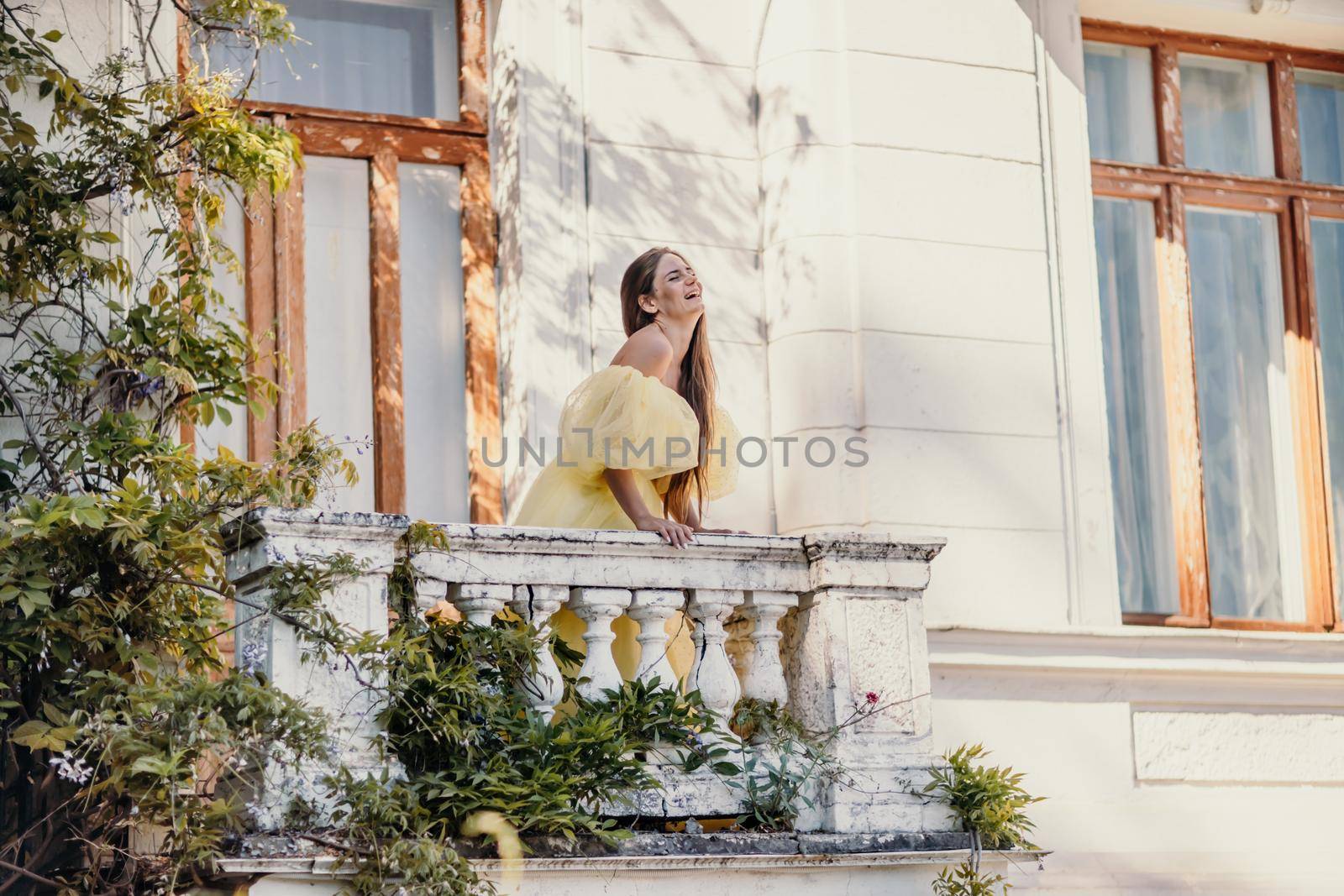 a beautiful smiling and kind woman in a gorgeous yellow dress stands on the balcony of an old vintage house by Matiunina