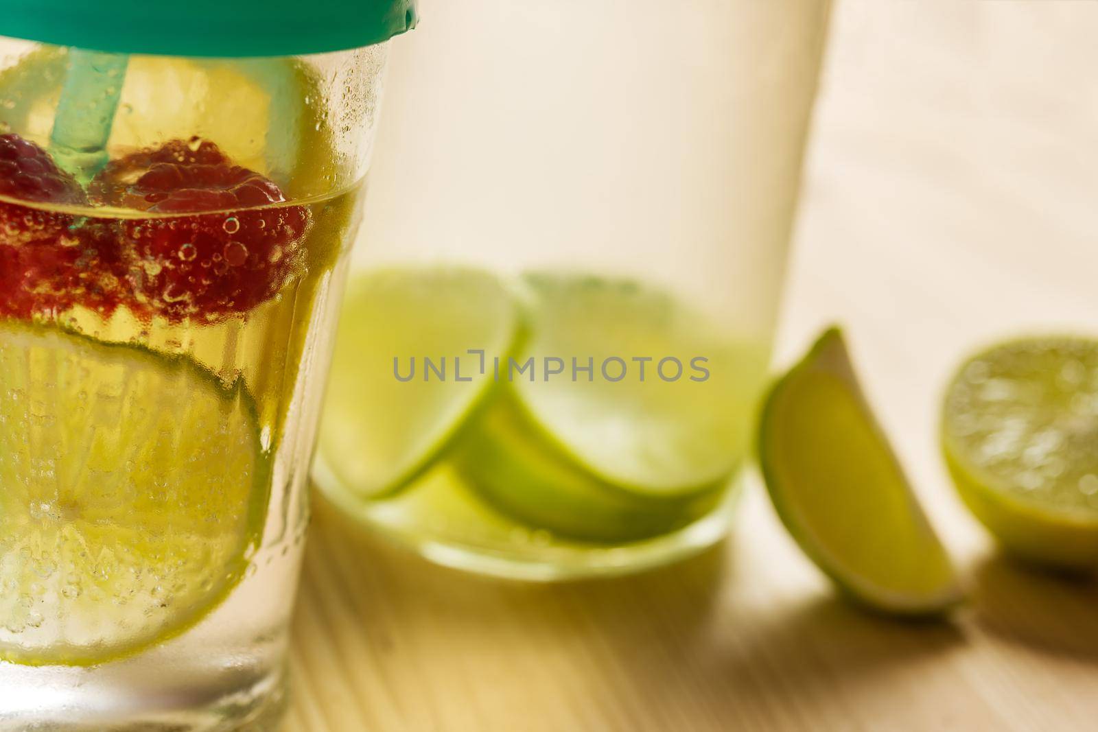 bottle and glass with cold water and slices of lime, lemon and red berries, illuminated by sunlight on a wooden table with some pieces of citrus, citrus summer refreshments background, copy space