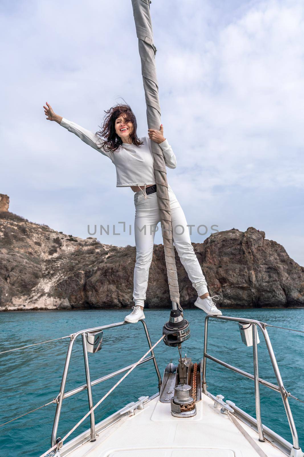 Woman standing on the nose of the yacht at a sunny summer day, breeze developing hair, beautiful sea on background.