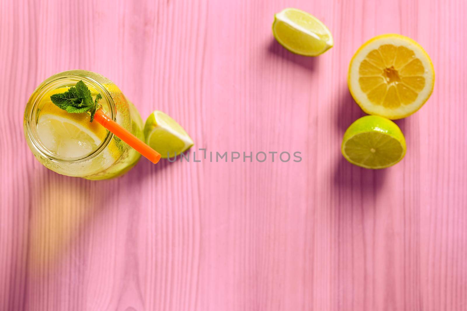 glass jar with homemade lemonade, mint and a cane, on the pink wooden table there are also wedges of lime and lemon