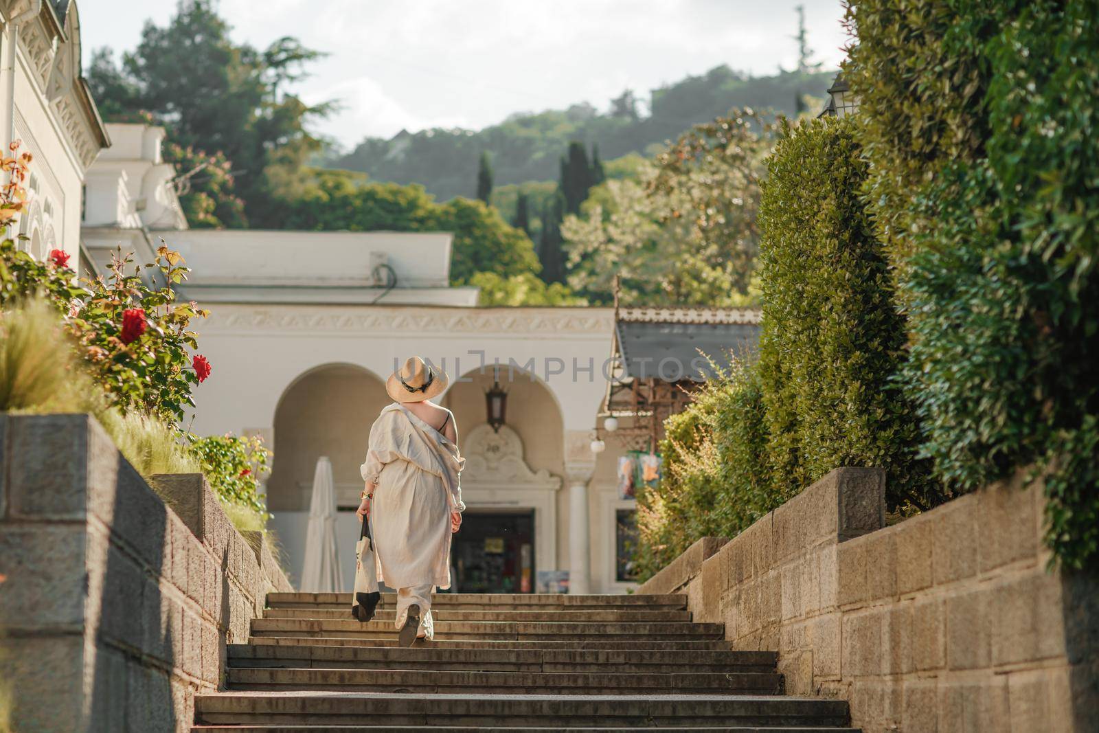 Woman on the stairs in the park. A middle-aged lady in a hat in a white outfit with a bag walks around the Livadia Palace by Matiunina