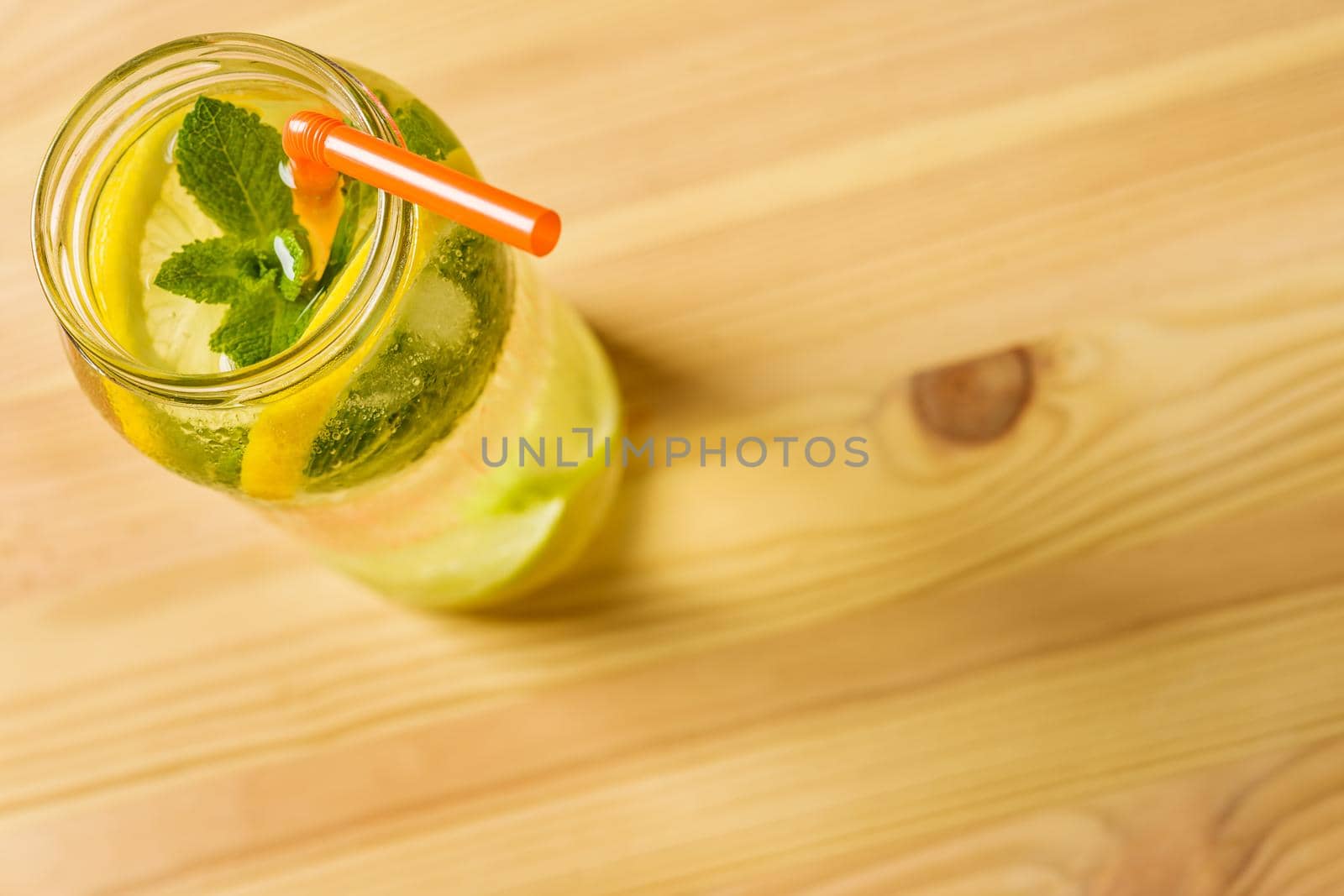 flat lay of homemade lemonade with sliced lemon, mint leaves and a cane to drink in a glass jar lit by sunlight, is on a wooden table, photo with copy space