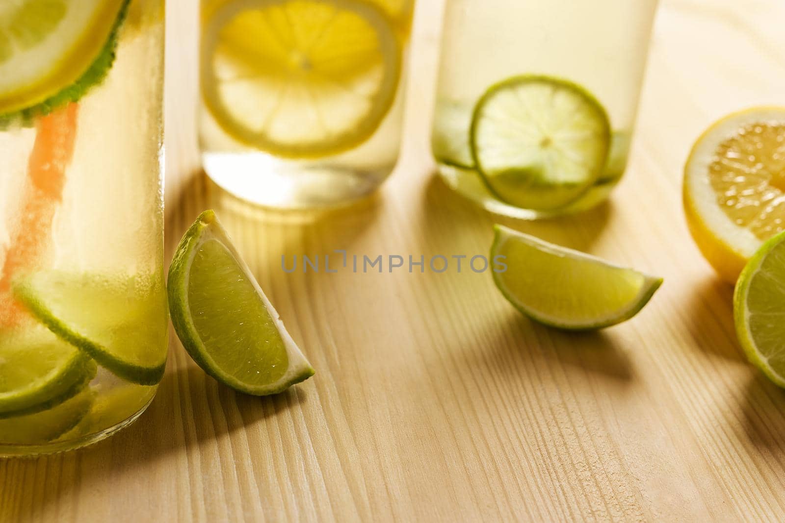 composition with copy space of three glass jars illuminated by sunlight with refreshing water with slices of lemon and lime, on the wooden table there are also pieces of citrus