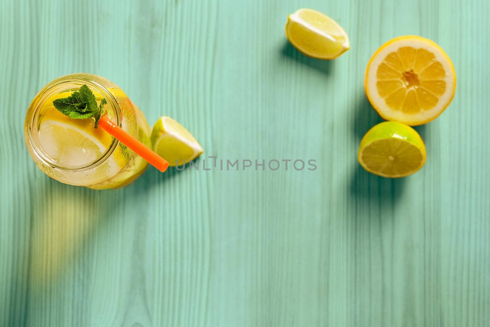 glass jar with homemade lemonade, mint and a cane, on the turquoise wooden table there are also wedges of lime and lemon