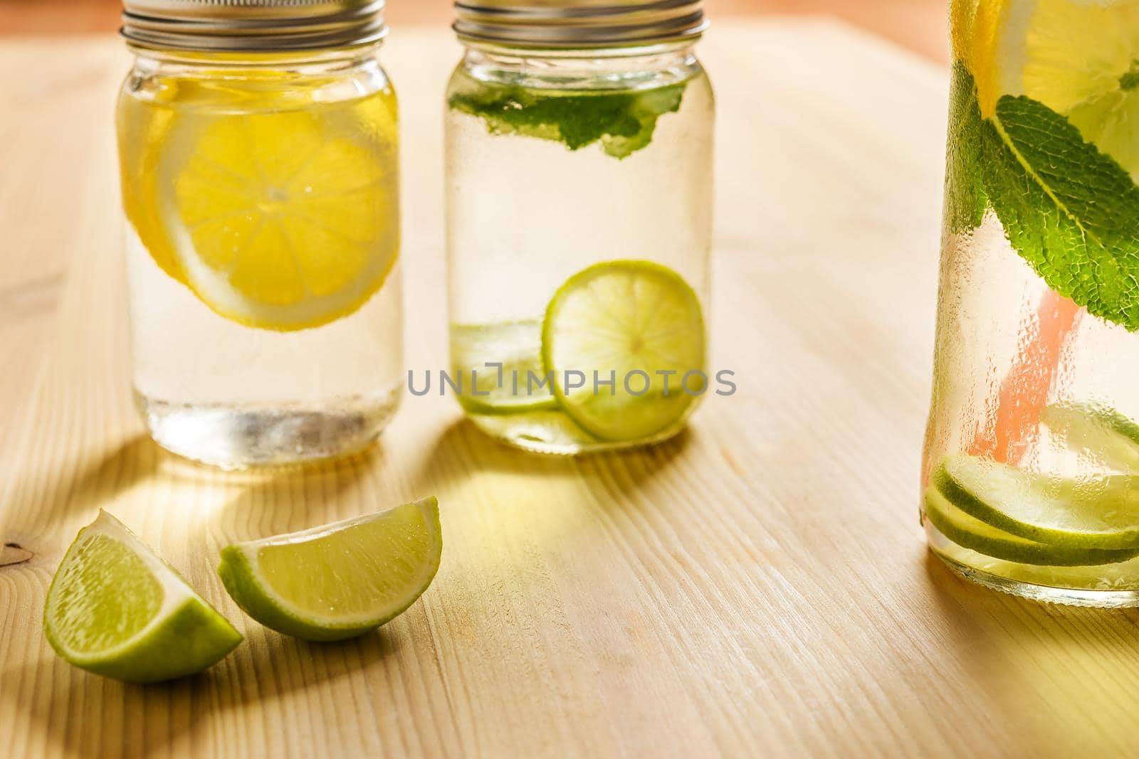 glass jar full of water with ice, slices of lemon and mint leaves, all is on a wooden table