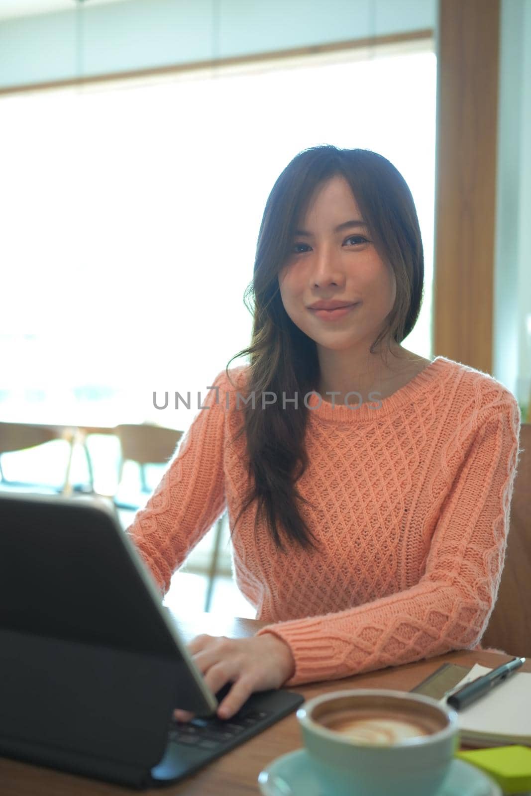 Young asian woman in warm sweater sitting in coffee shop and smiling to camera.