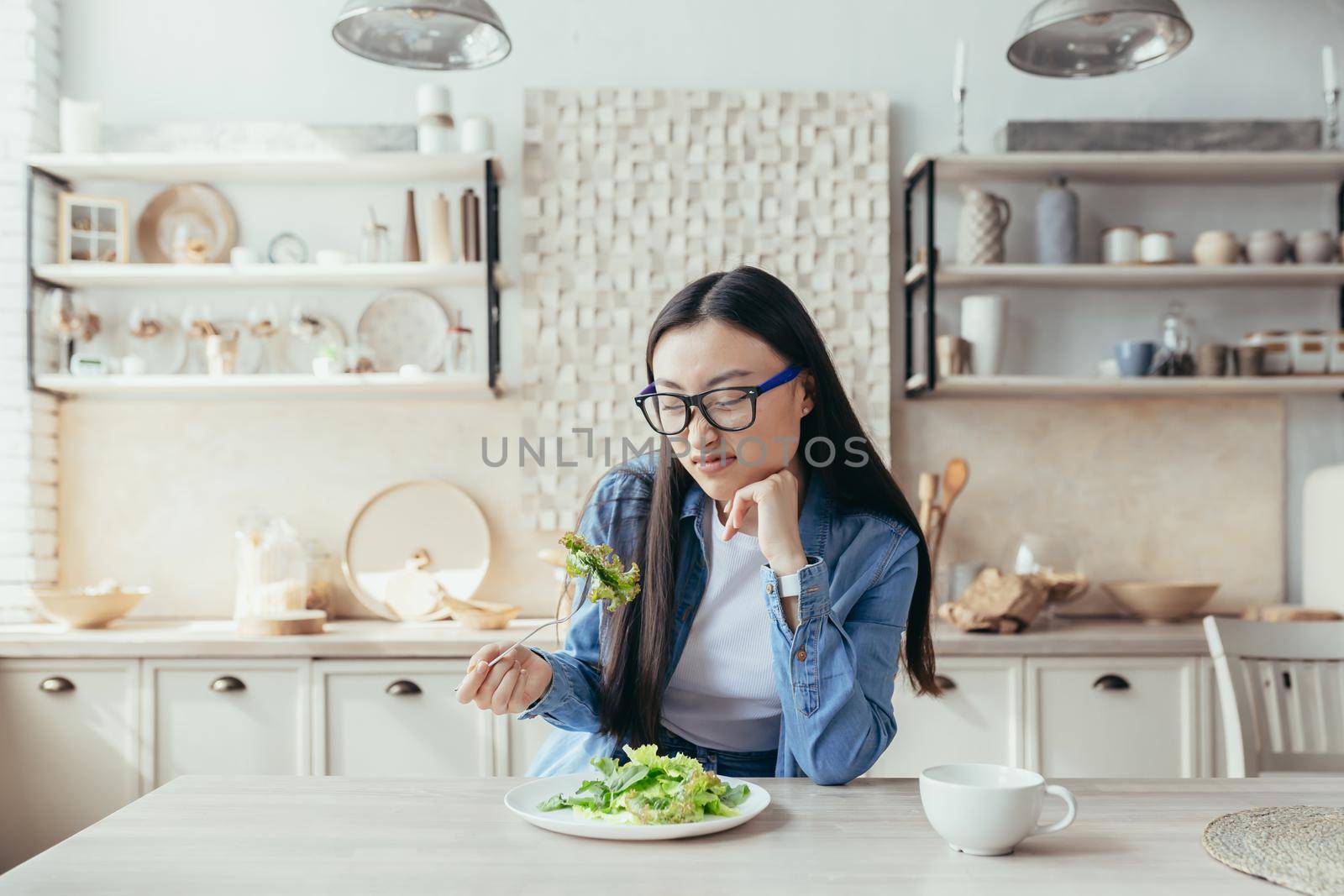 Young asian woman unhappy with diet in kitchen, woman eating healthy food, trying to eat salad and healthy food, teenager at home.