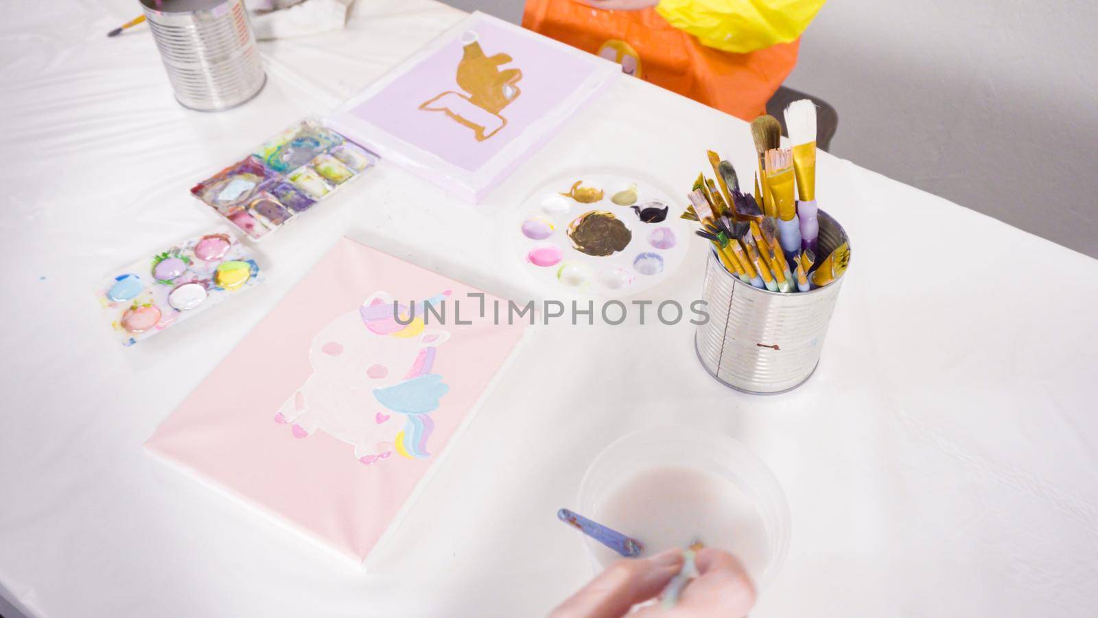 Little girl painting with acrylic paint on canvas with her mother for a distant learning art project.