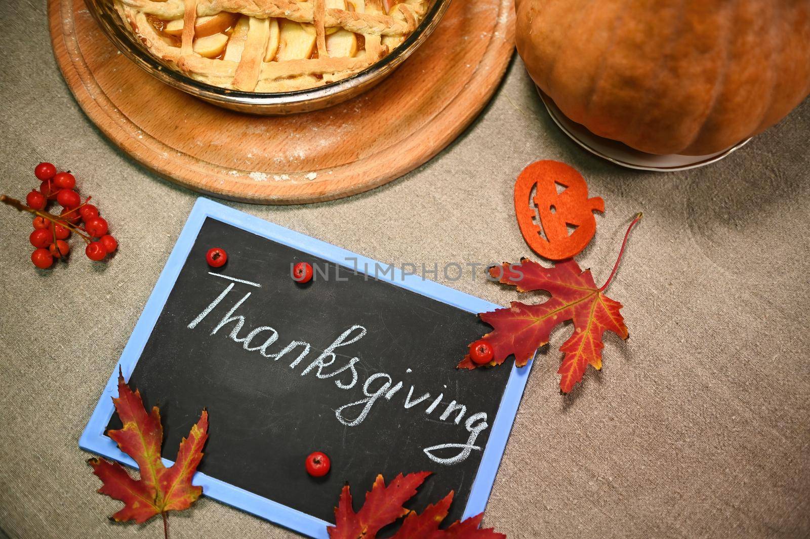 Flat lay. Chalk lettering Thanksgiving on a black board with maple leaves, pumpkin and Thanksgiving pie with flaky crust by artgf