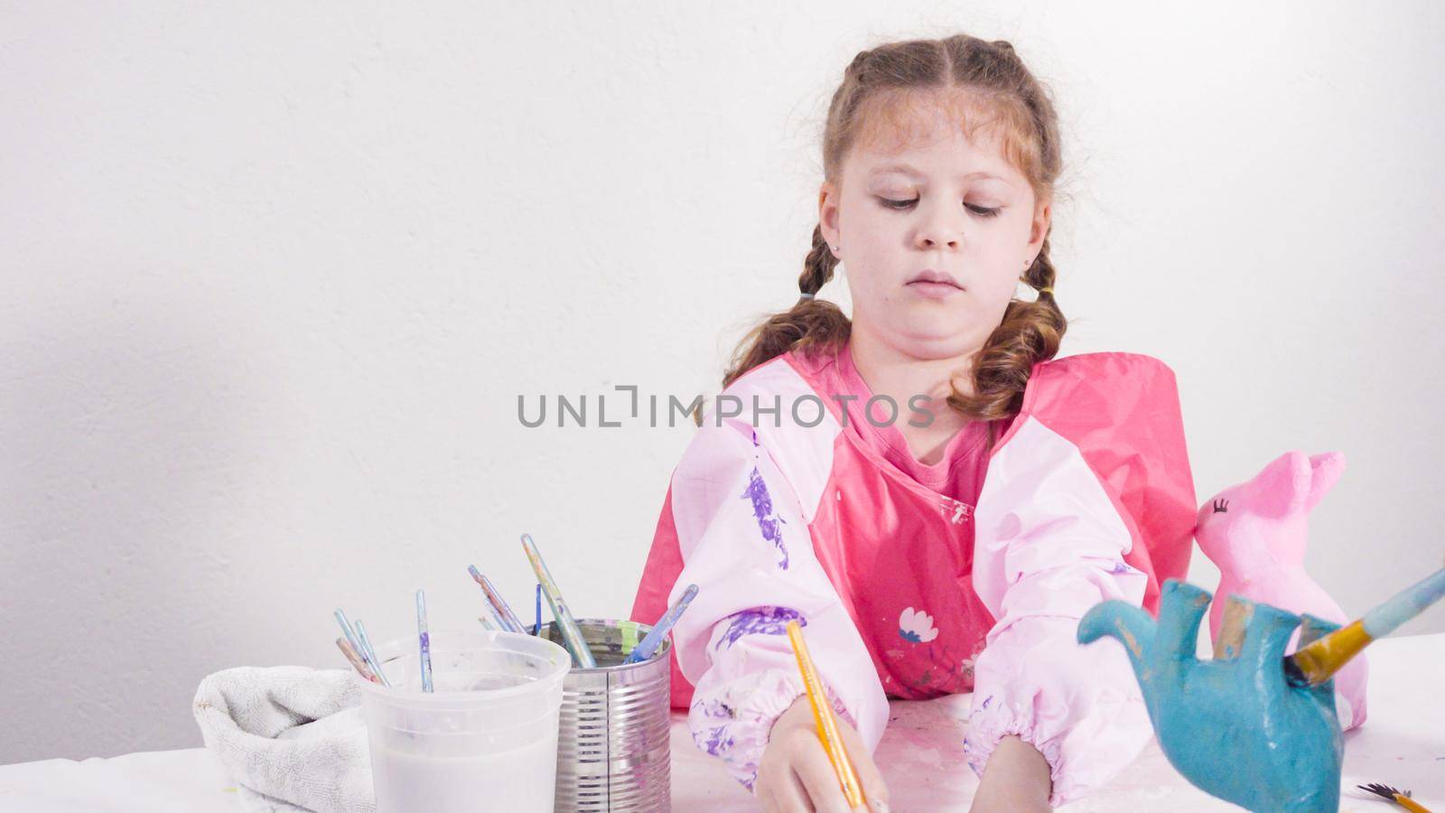 Little girl painting paper mache figurines with acrylic paint for her homeschooling art project.