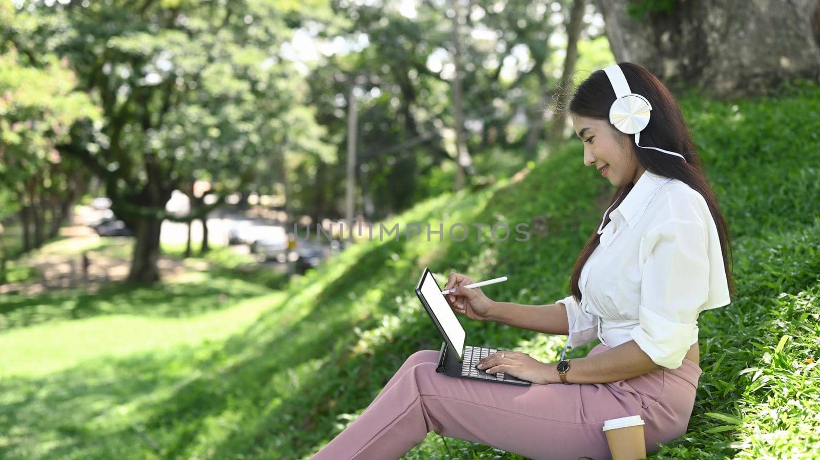 Young asian woman wearing headphone and working with computer tablet in the park.